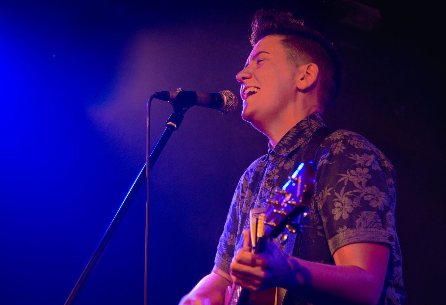 Musician performs on stage bathed in deep blue concert lighting.