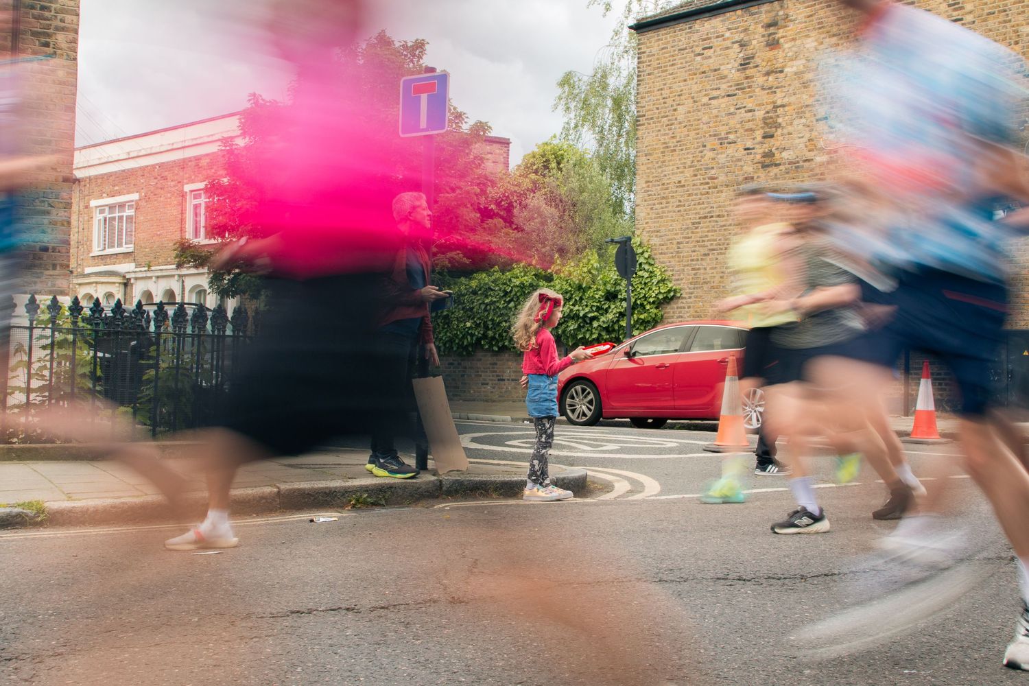 Runners in motion blur pass a spectator releasing pink smoke during a street race in an urban setting.