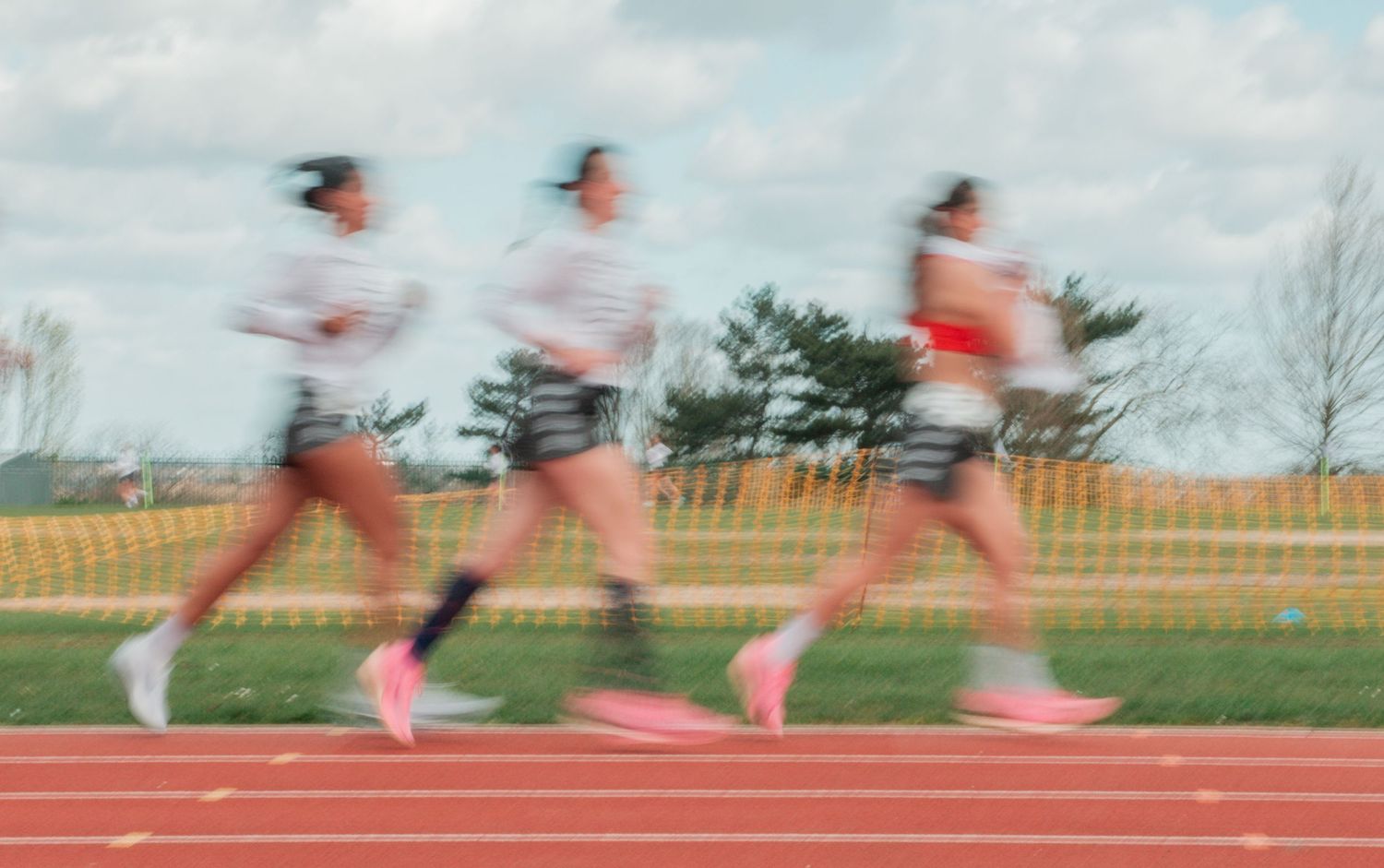 Three female athletes running on a red track, captured with motion blur effect showing speed and athleticism.
