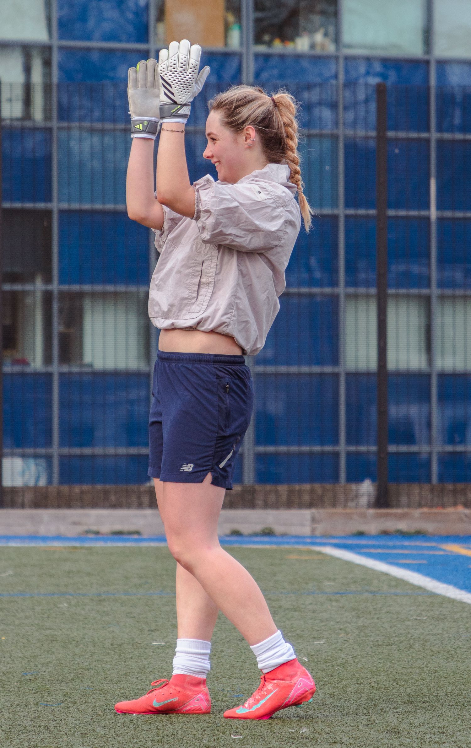 Soccer player wearing white socks and bright red cleats stands on an artificial turf field near blue stadium walls.