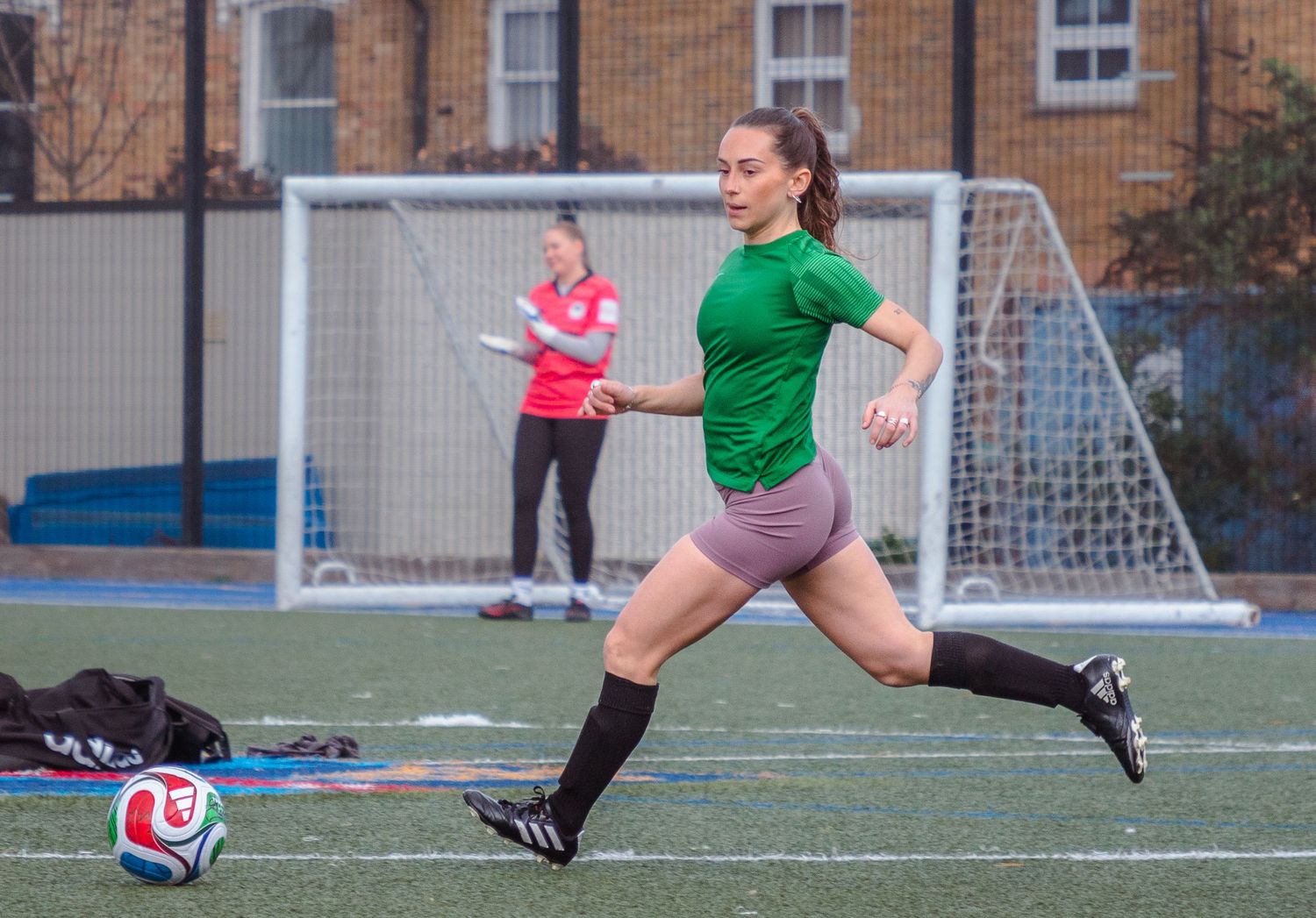 Soccer player in green jersey and black shorts performs a kicking motion on outdoor turf field.