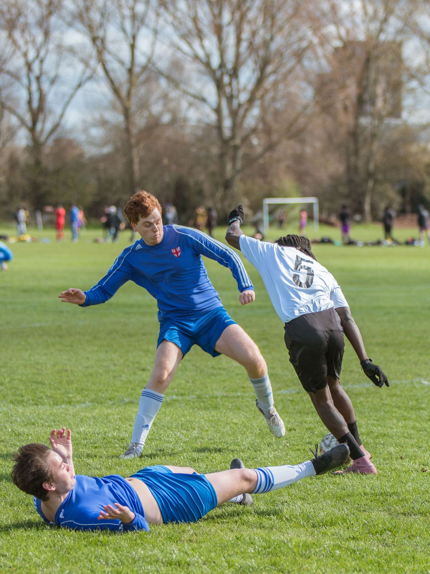 Soccer players collide and fall dramatically on a grassy field during an intense match on a sunny day.
