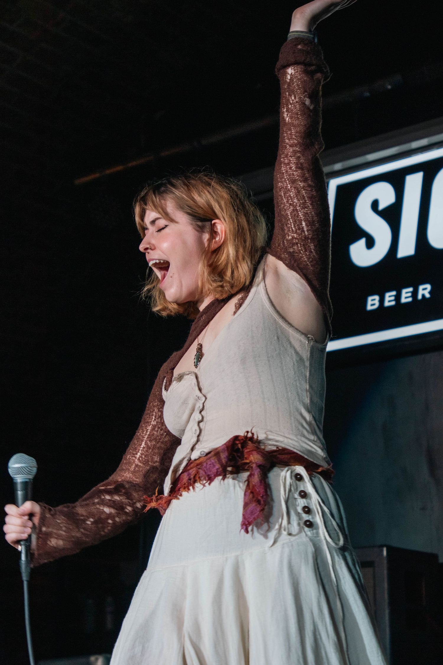 Performer in white dress dances energetically on stage during live performance.