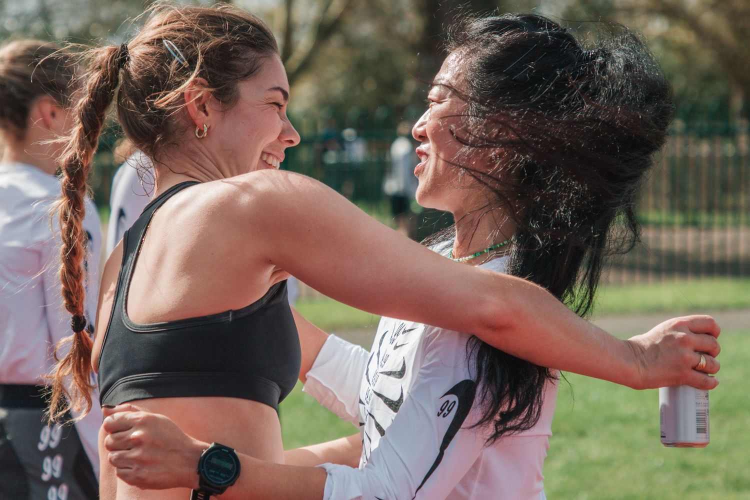 Two women runners embrace and laugh after a race outdoors on a sunny day.