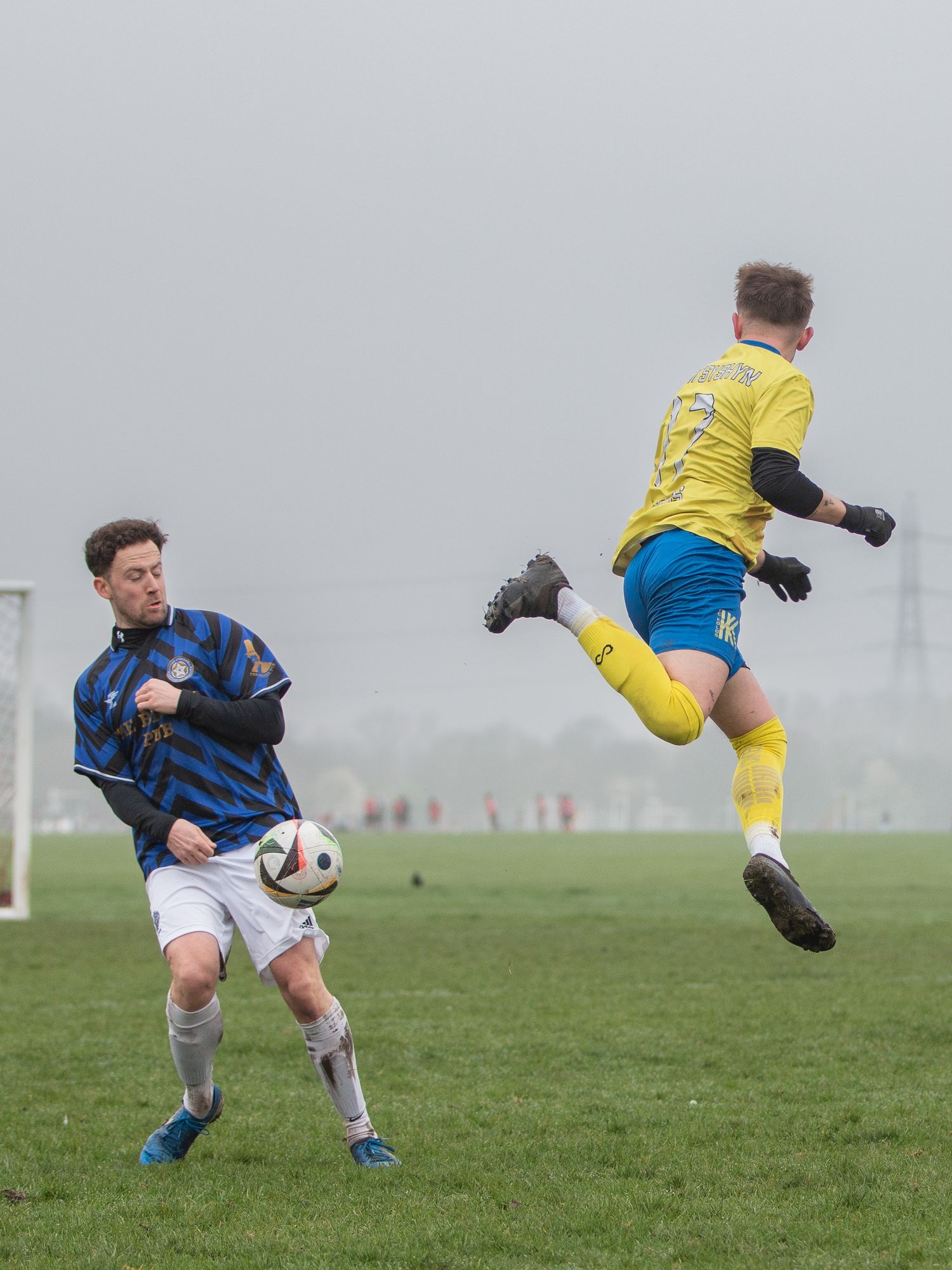 Soccer players compete for possession of the ball during a foggy match on a grass field.