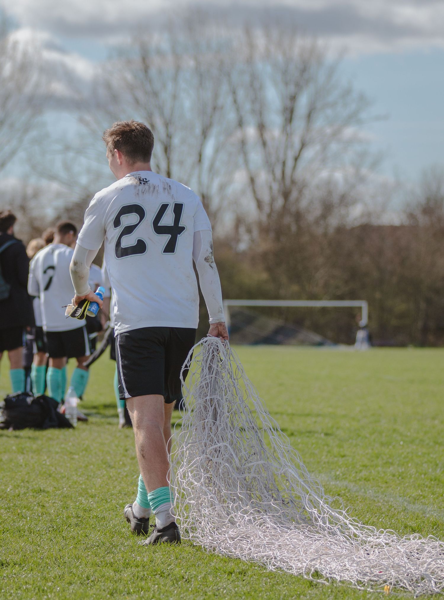 Soccer players wearing white jerseys with numbers 24 and 21 run across a grassy field with streamers trailing behind them.