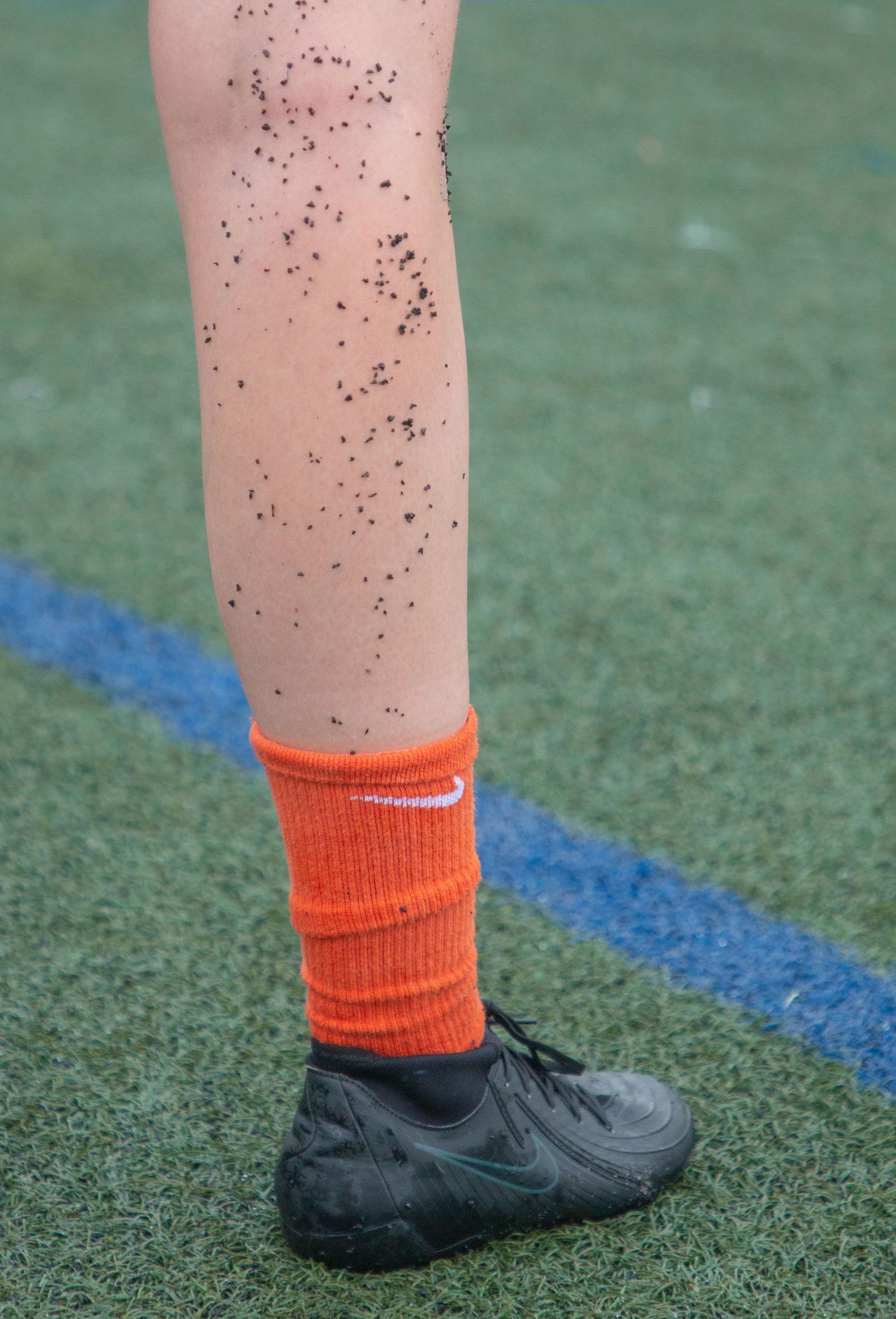 Close-up of leg wearing orange sock and black shoe on artificial turf.