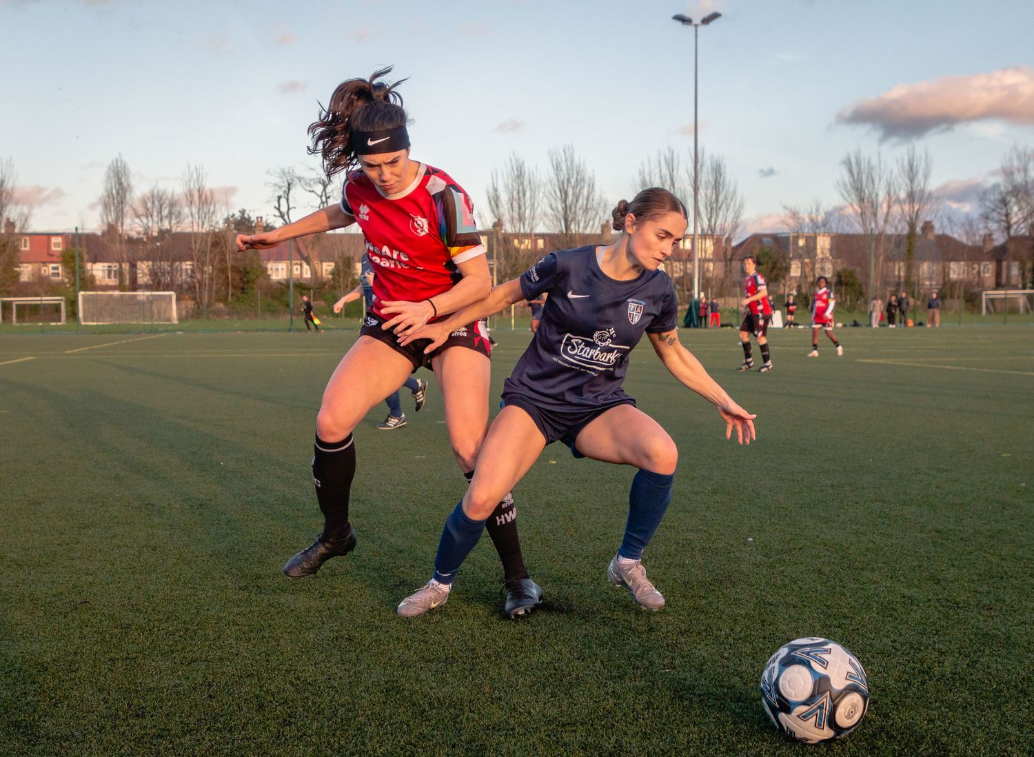 Soccer players compete for possession of the ball during an intense match on a grass field at sunset.