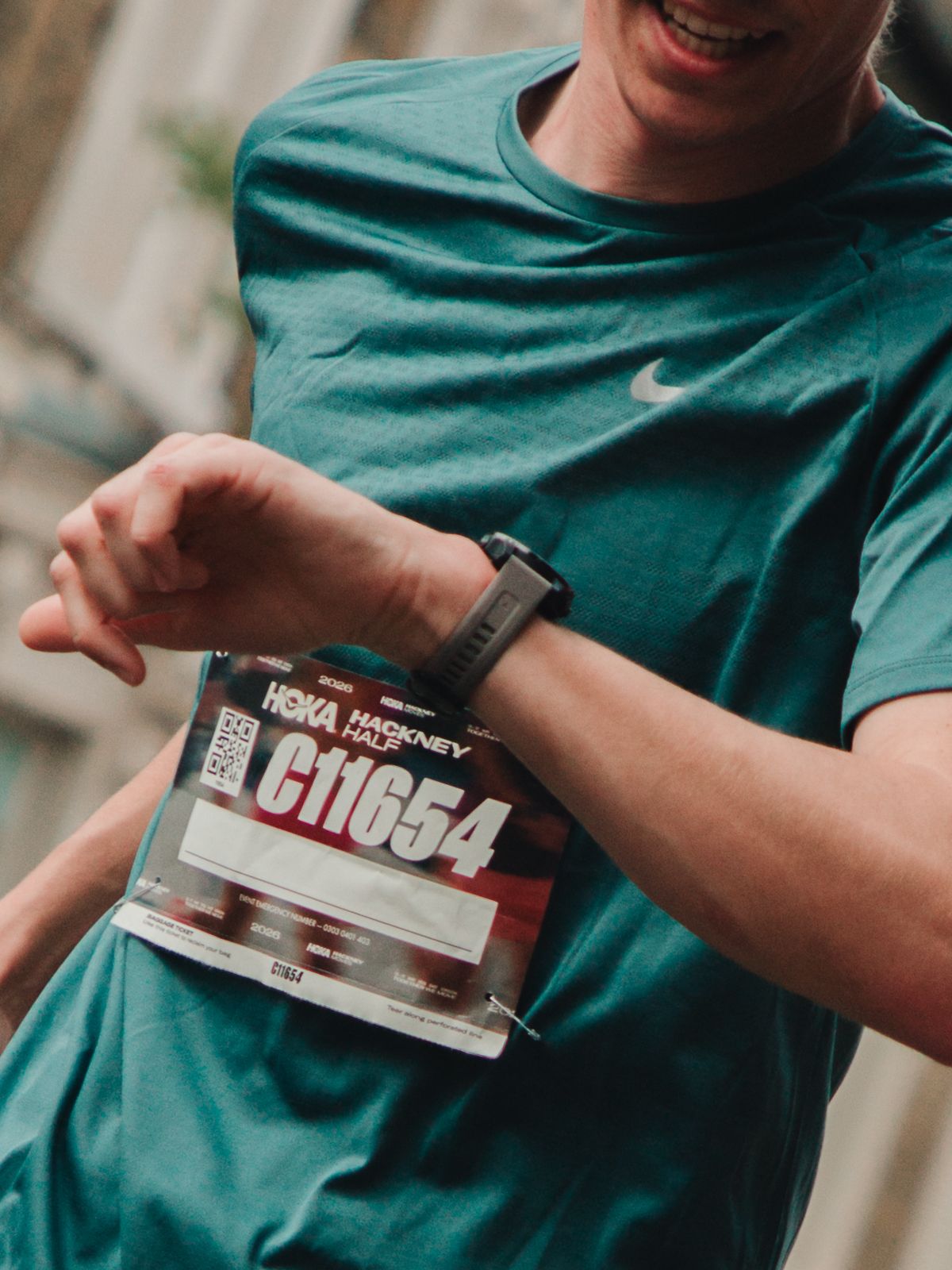 Runner checking smartwatch wearing teal Nike shirt with race bib C11654 from Hackney Half Marathon.