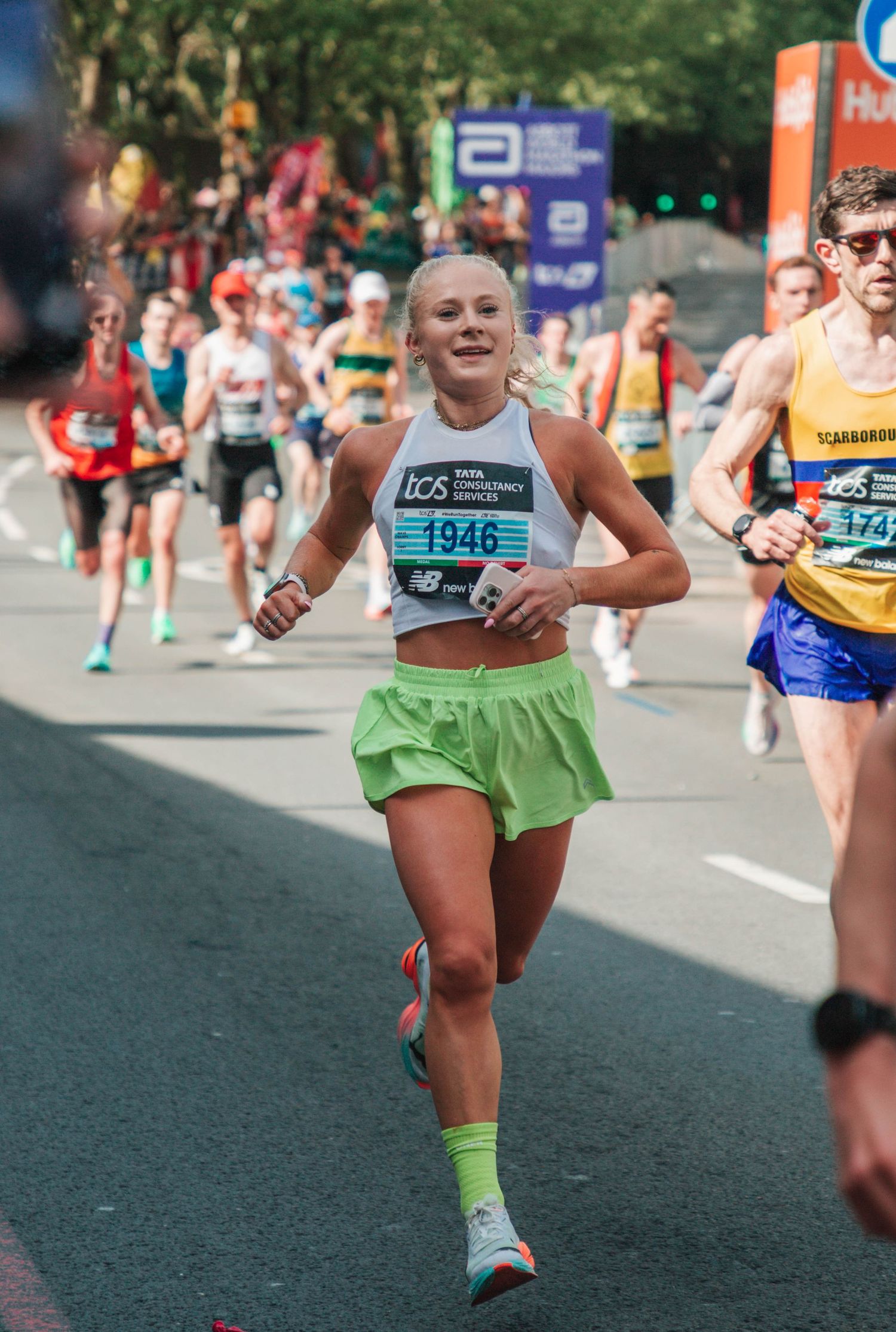 Female runner wearing bib 1946 competing in a road marathon, dressed in green skirt and white crop top.