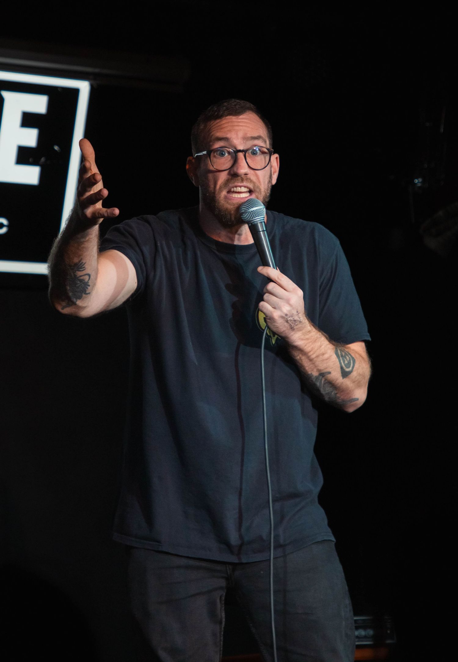 Stand-up comedian performing on dark stage with microphone.