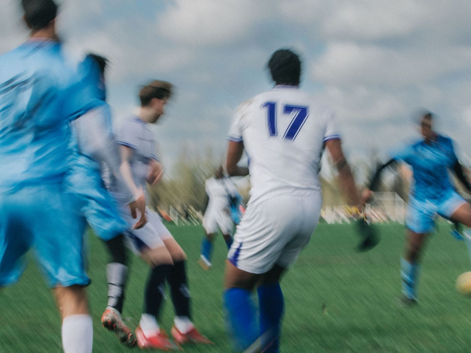 Soccer players in white and blue uniforms compete for the ball during an intense match on a grass field.
