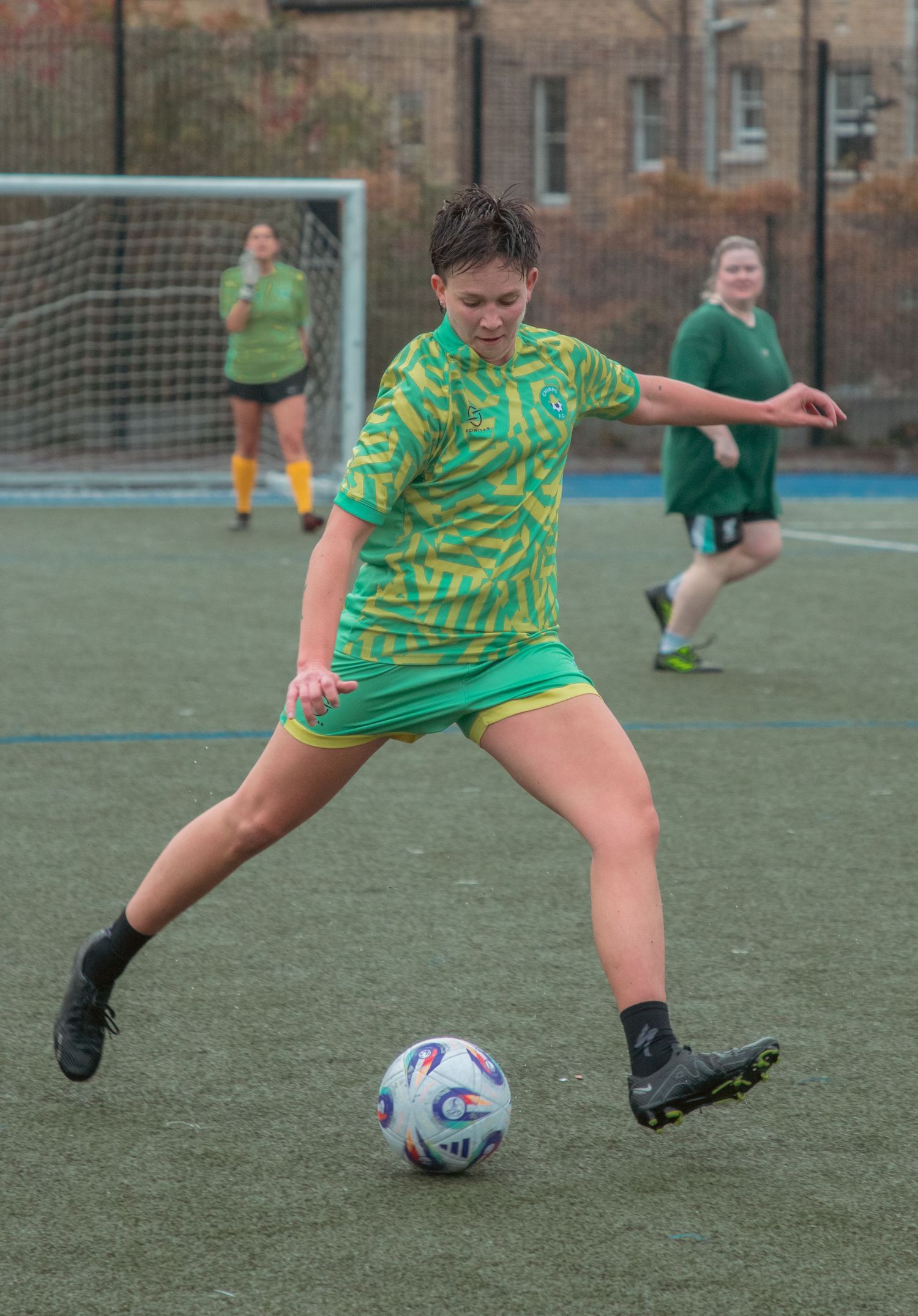 Soccer player in yellow and green jersey kicks ball during game on artificial turf.