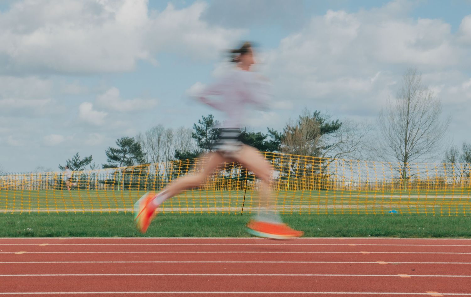 Blurred motion shot of a runner sprinting on a red athletic track under a cloudy sky.