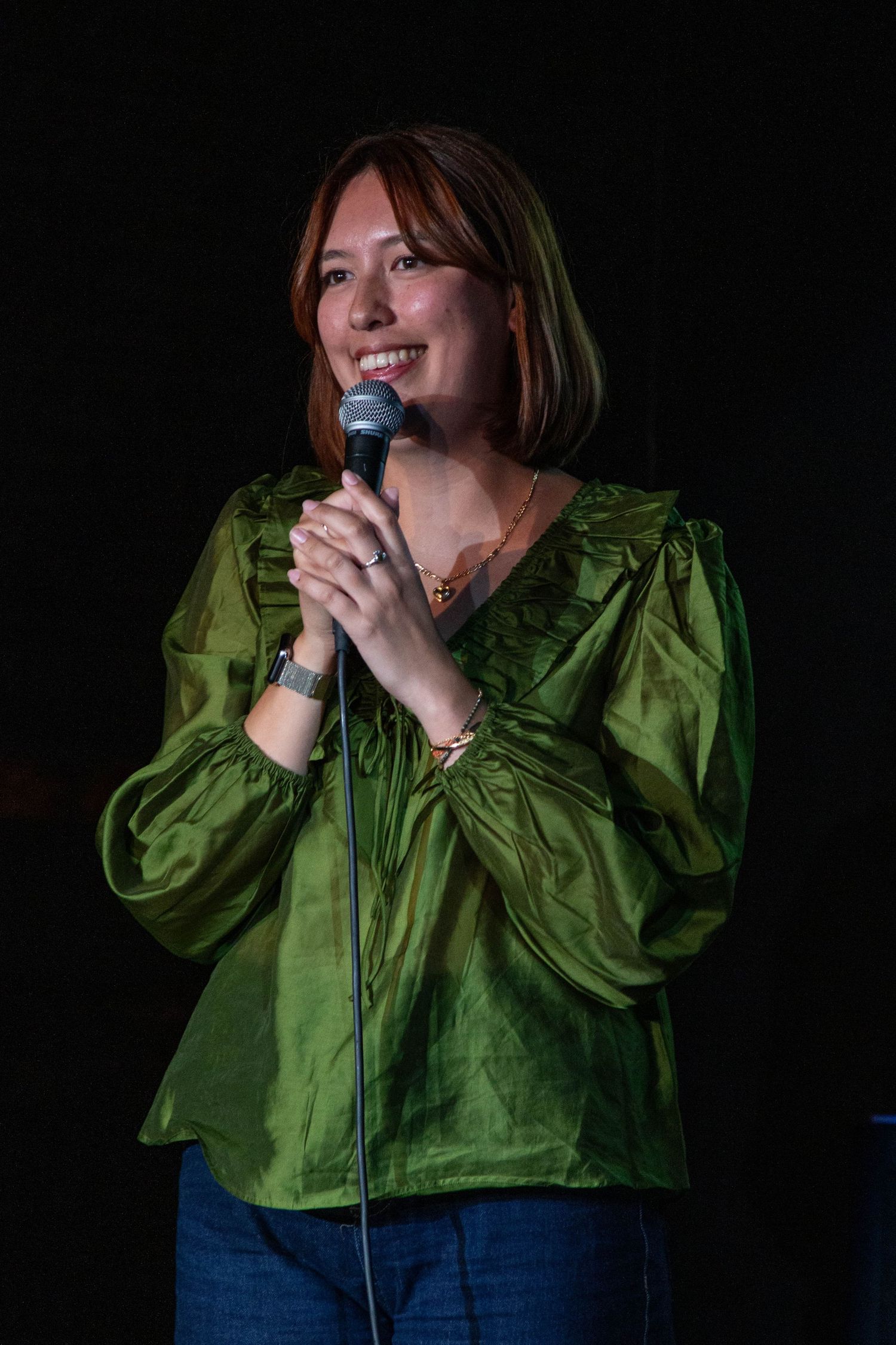Performer in green puffy blouse sings emotively against dark background.