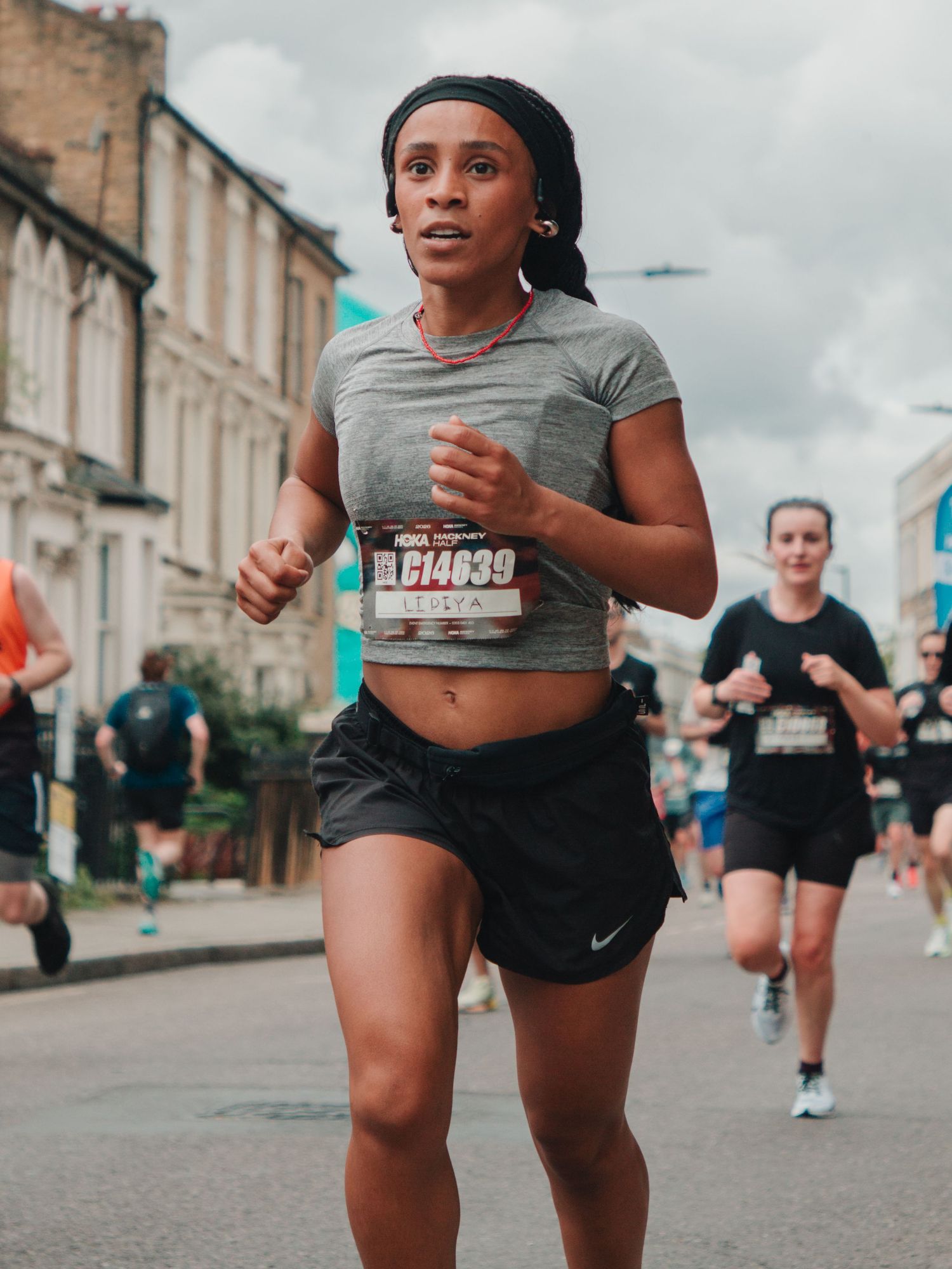 Woman running in a street marathon wearing a gray crop top, black Nike shorts, and race bib number 614039.