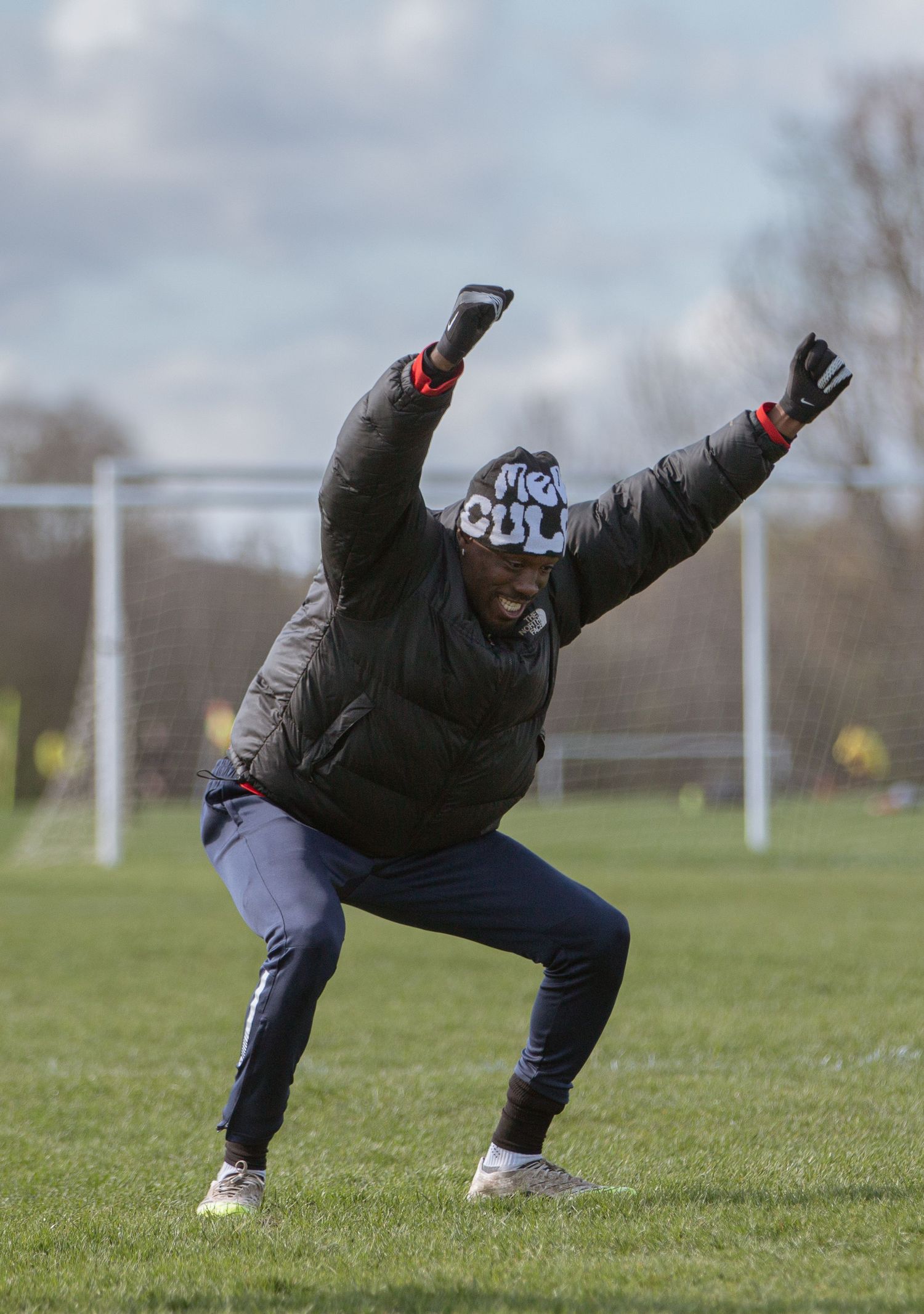 A sequence of action shots showing a person in a black coat performing a backflip on a grassy sports field.