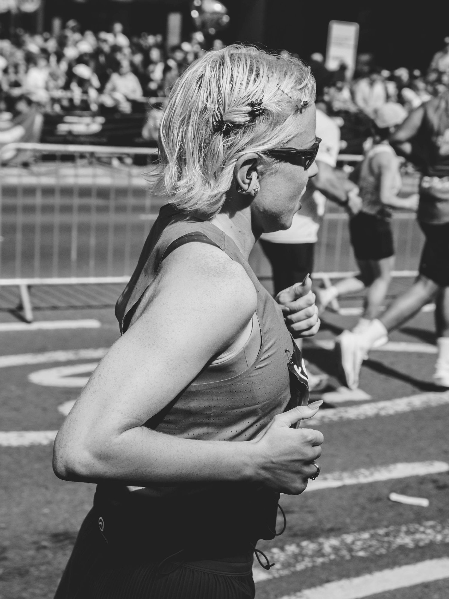 Black and white photo of a blonde woman running a marathon wearing sunglasses and earphones in an urban race.