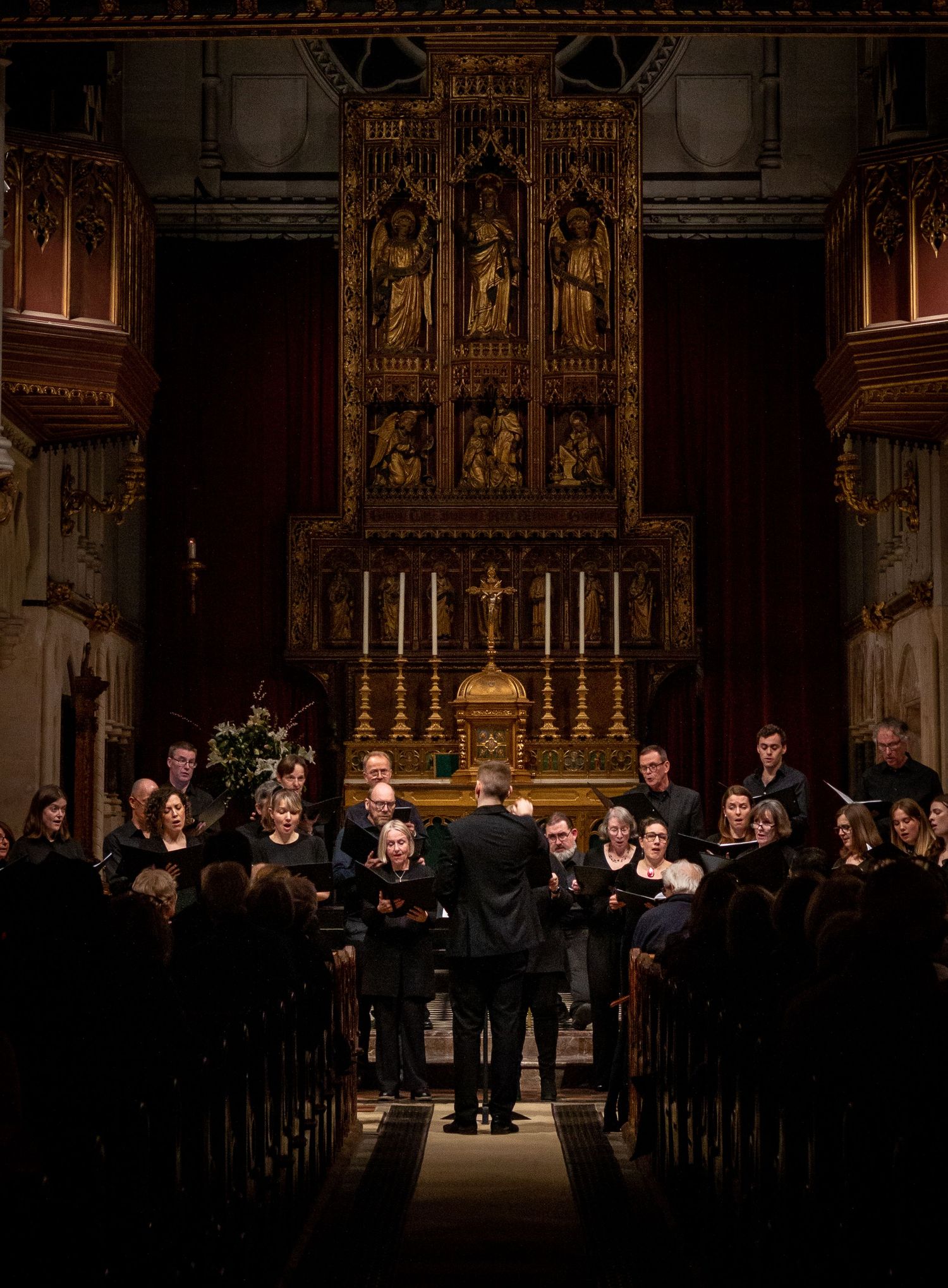 A choir performs in a darkly lit church with ornate golden altars and religious decorations in the background.