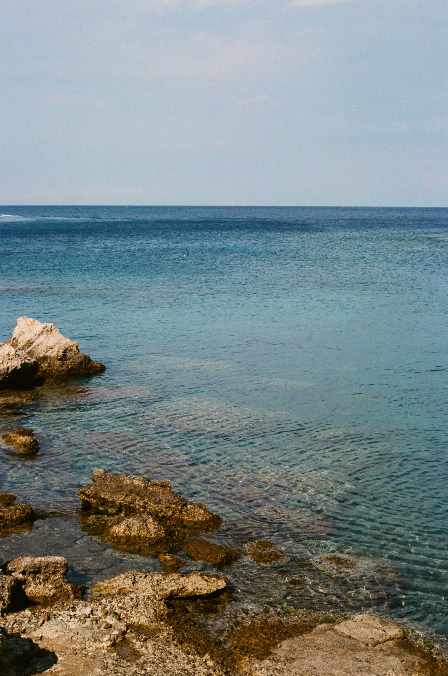 Crystal clear turquoise waters meeting rocky shoreline under bright blue sky.