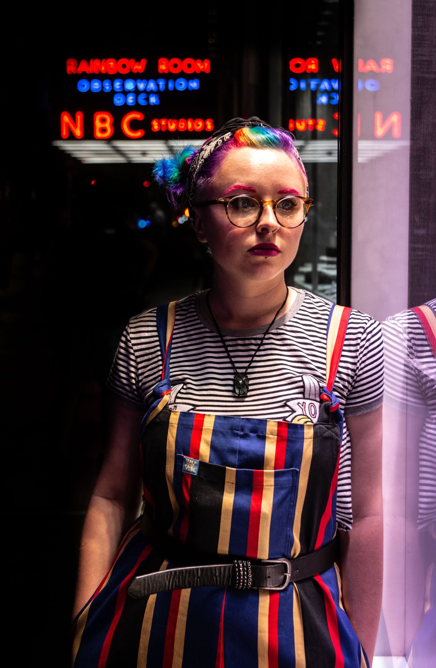 Neon signs illuminate storefront window display with striped clothing in evening light.