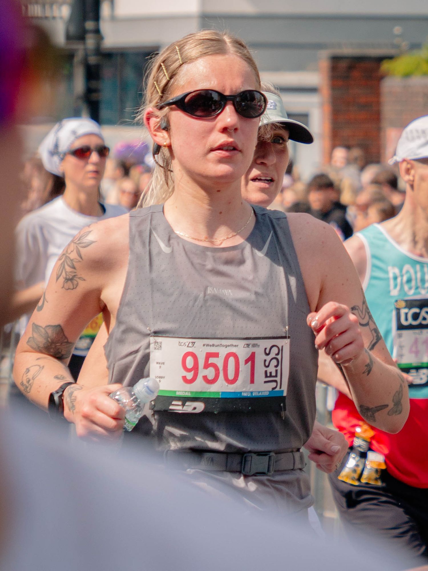 Female marathon runner wearing bib number 9501 and sunglasses races through a crowded city street event.