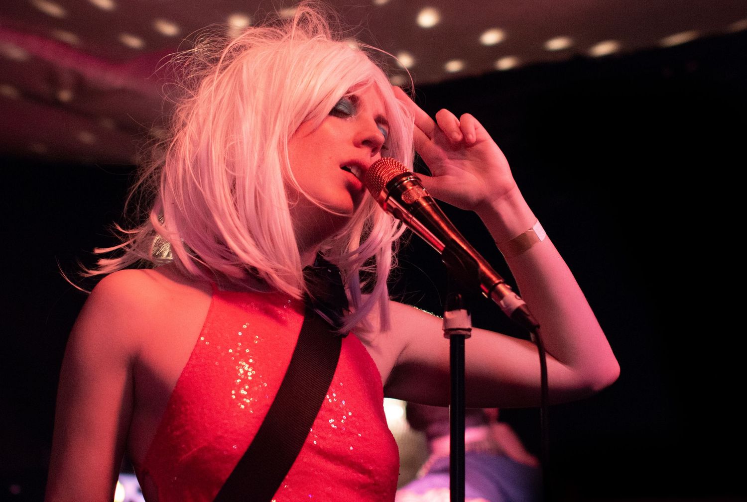 Singer in red dress performs passionately on stage with dramatic lighting.