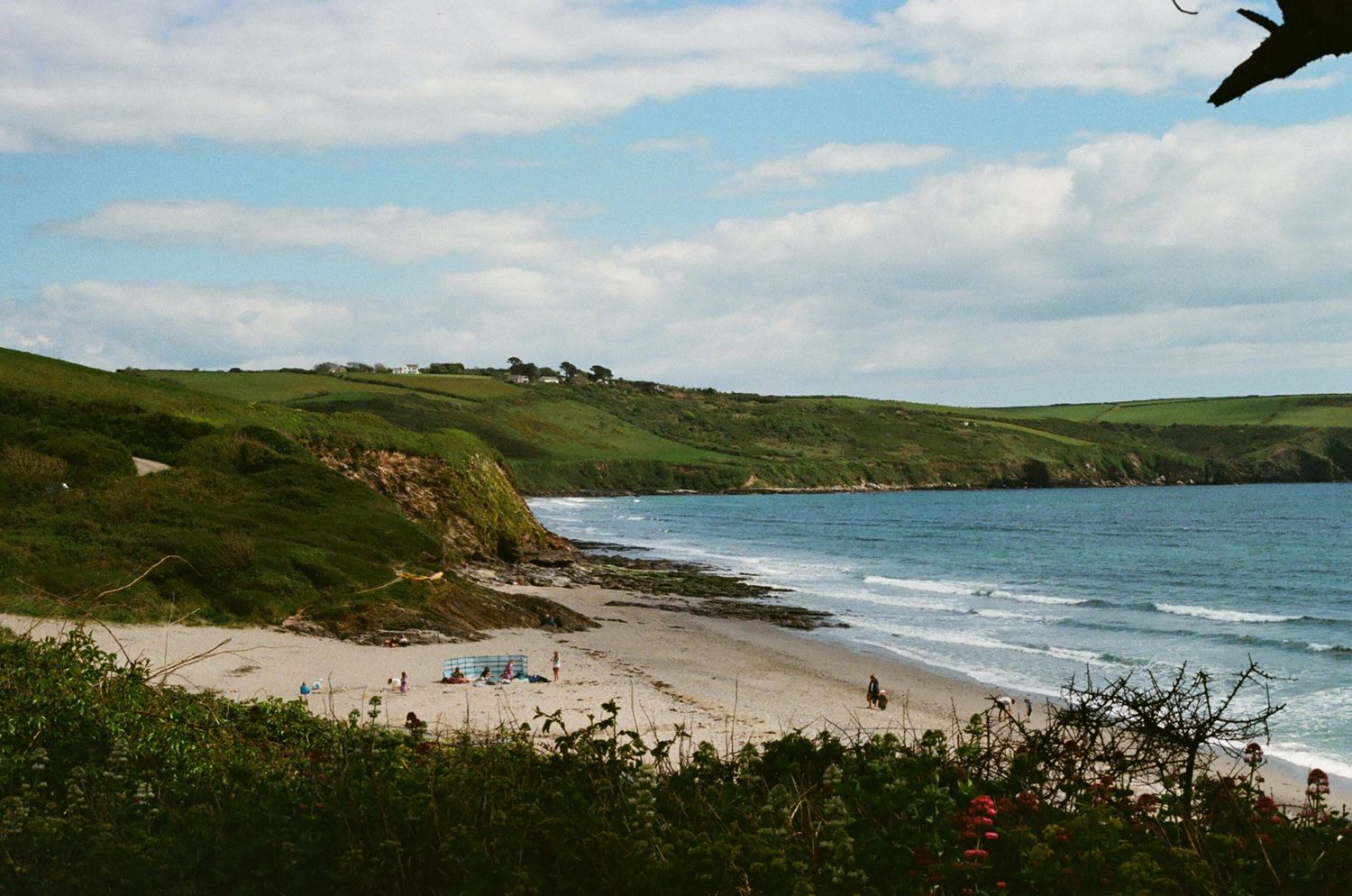 Scenic coastal beach cove with sandy shore and green cliffs under partly cloudy sky.