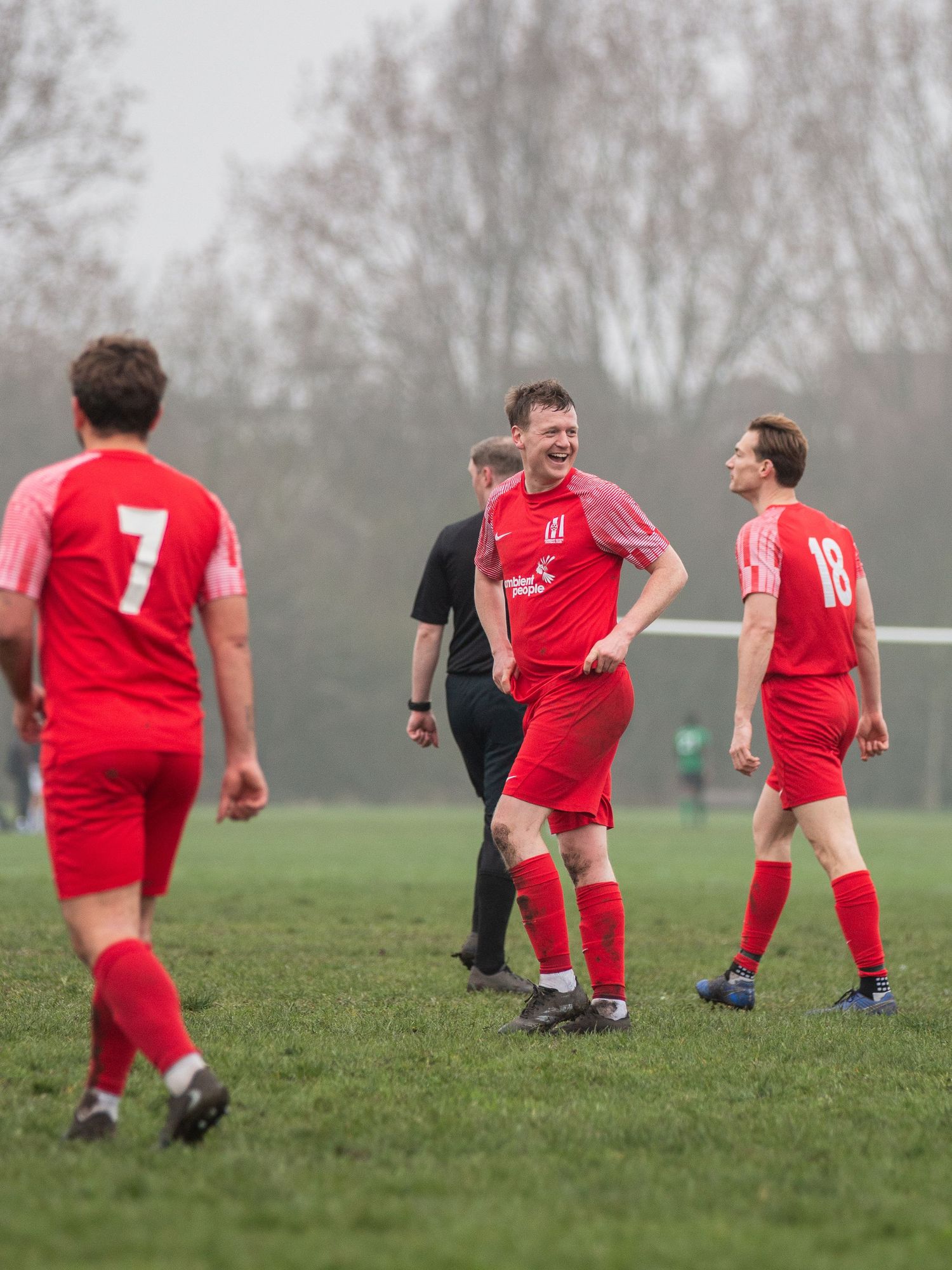 Soccer players in red uniforms perform dynamic stretching exercises on a foggy grass field during warmup drills.