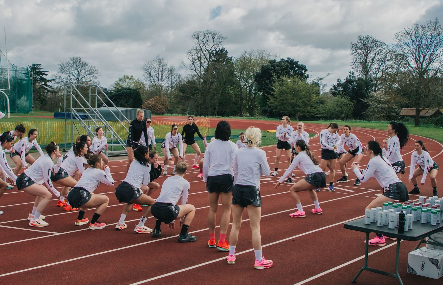 Female athletes in white uniforms warming up on a red running track during outdoor sports training session.