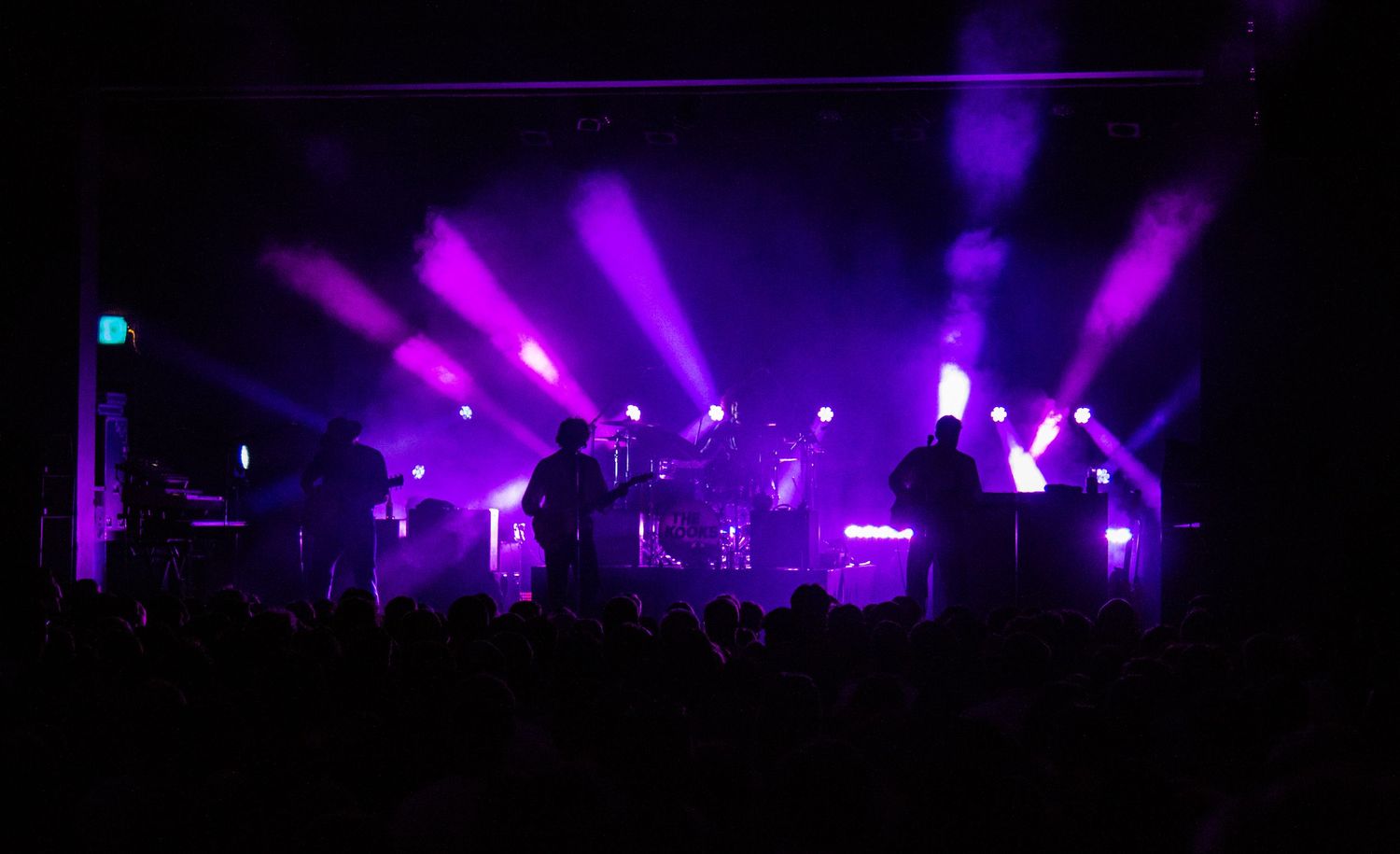 Concert venue illuminated with purple stage lights creating atmospheric silhouettes.