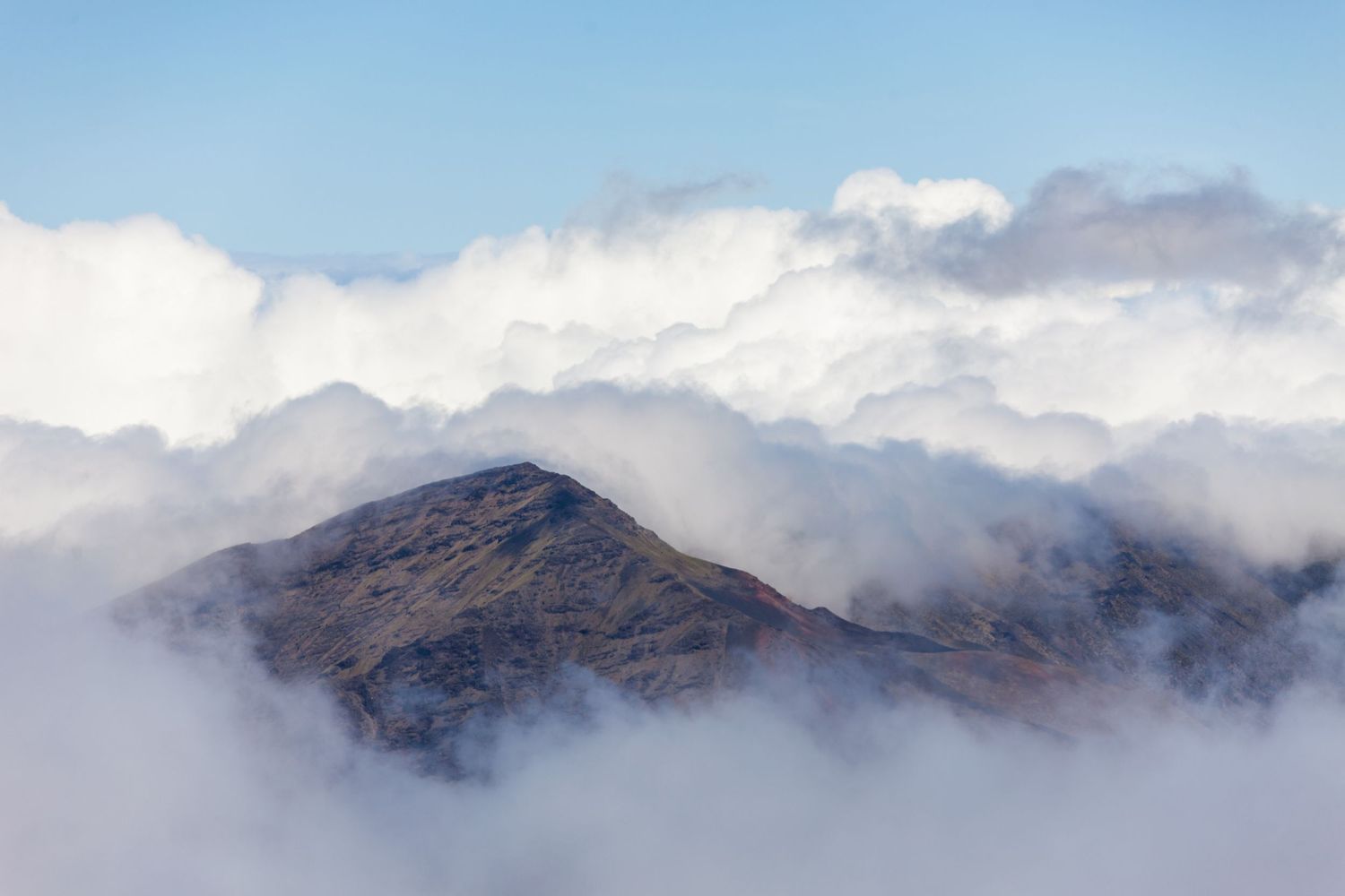 Misty mountain peak emerges through dramatic cloud cover against a blue sky.