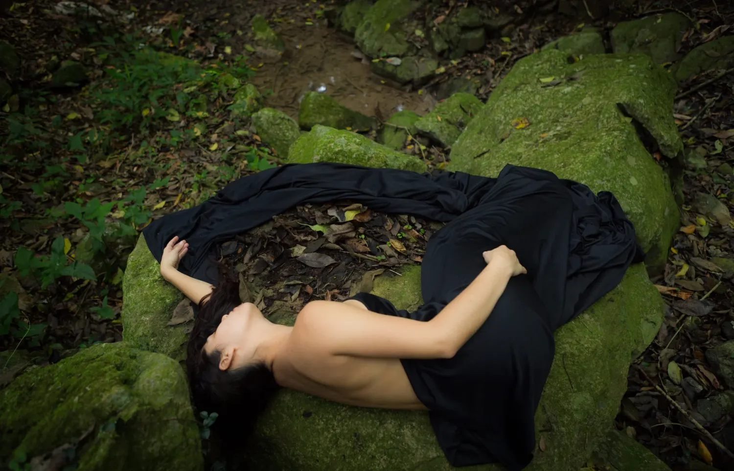 Figure lying on mossy rocks in a dramatic nature setting.
