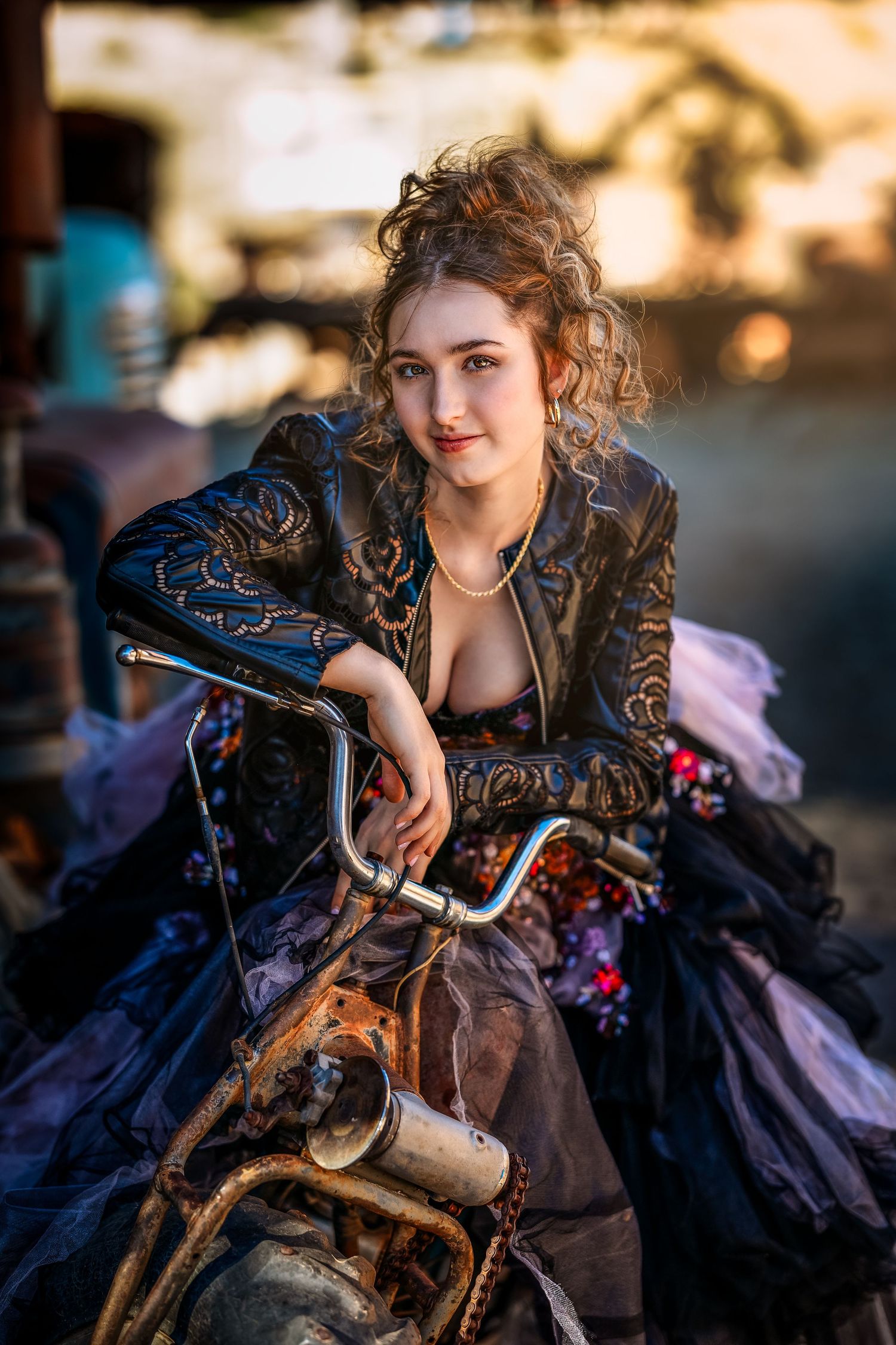 Young woman in steampunk Victorian gown and embroidered jacket poses on rustic vintage motorcycle outdoors.