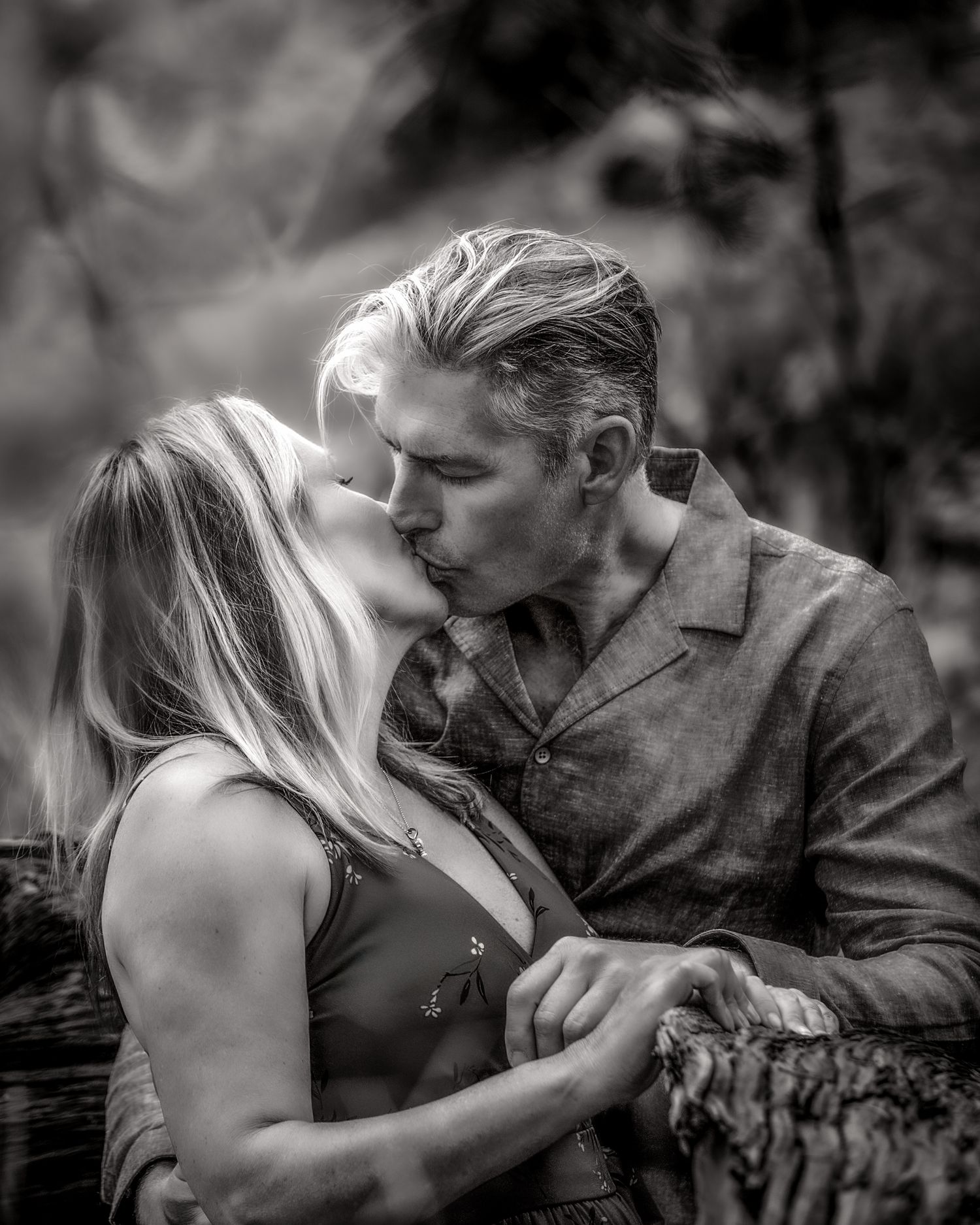 Black and white romantic portrait of a couple kissing outdoors in a natural wooded setting.