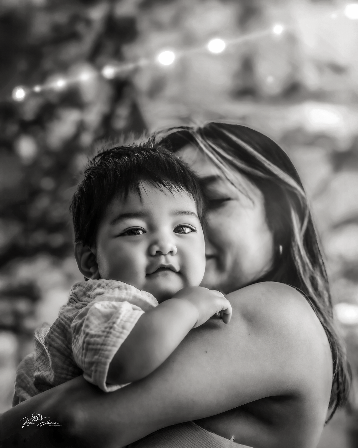 Black and white photo of a woman tenderly kissing a cute baby she holds in her arms.