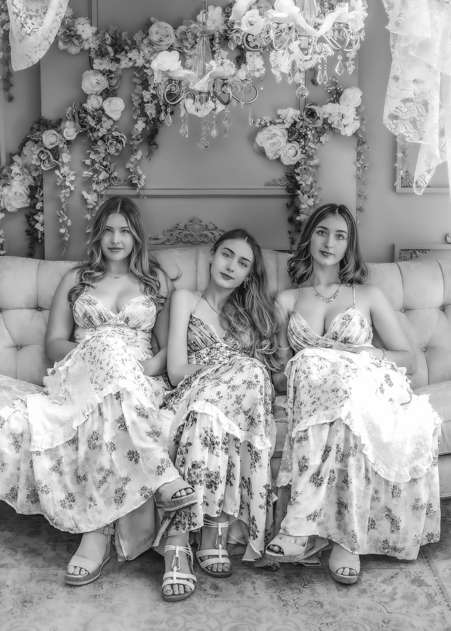 Three young women in floral dresses seated together on tufted sofa, black and white photo.