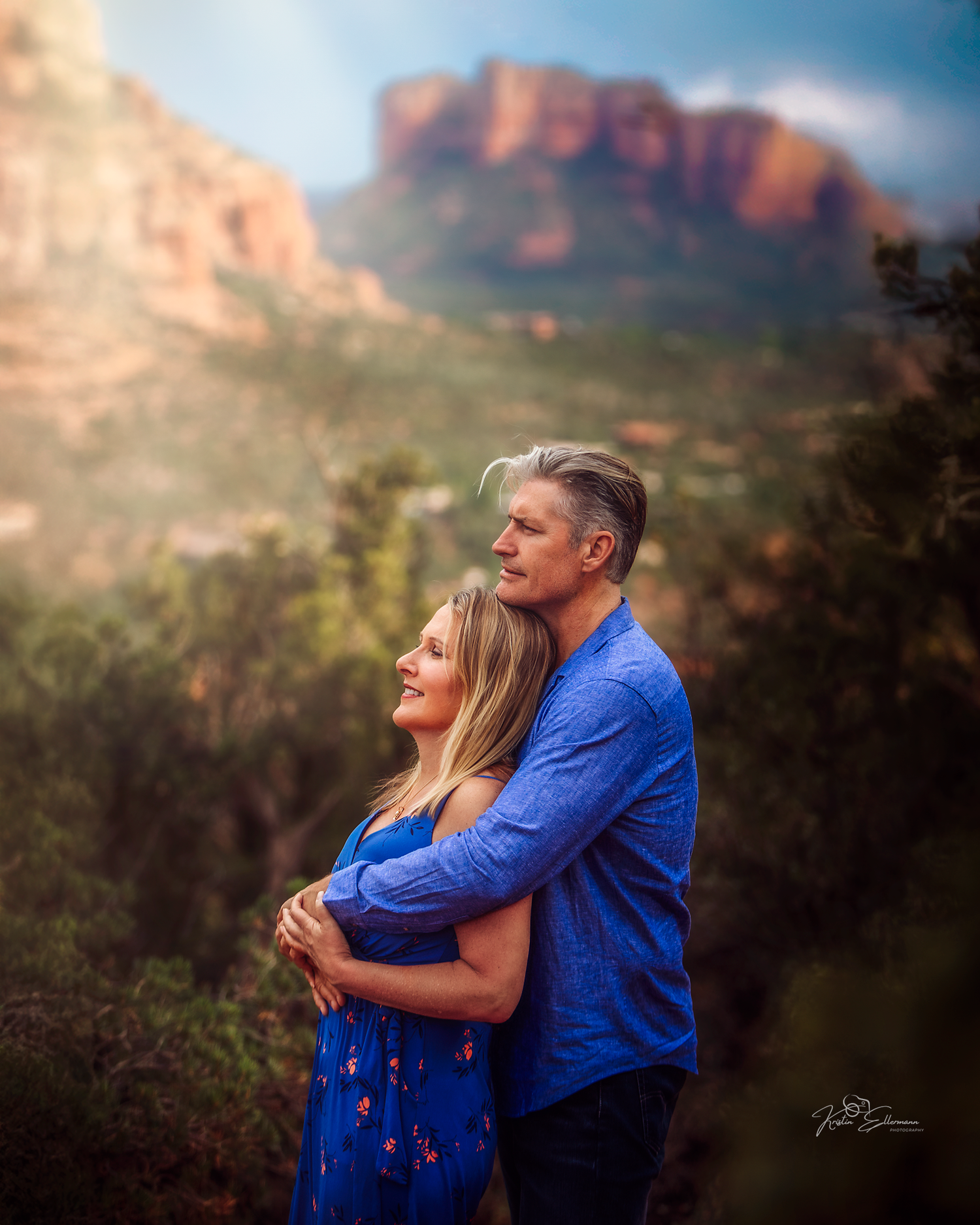 Couple embracing with red rock formations and lush greenery in Sedona Arizona at sunset.