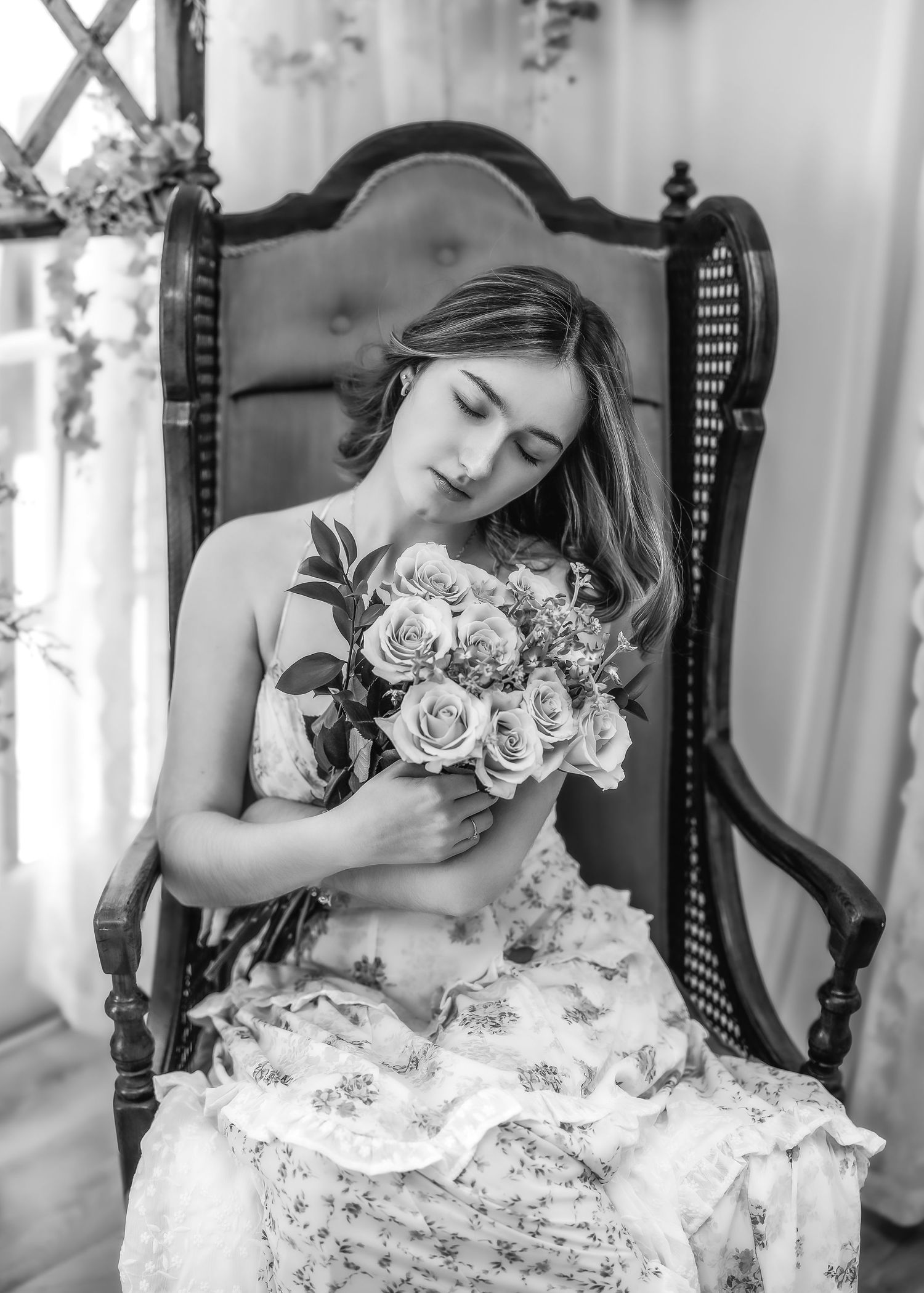 Young woman in floral dress holding bouquet of roses with eyes closed, black and white portrait.