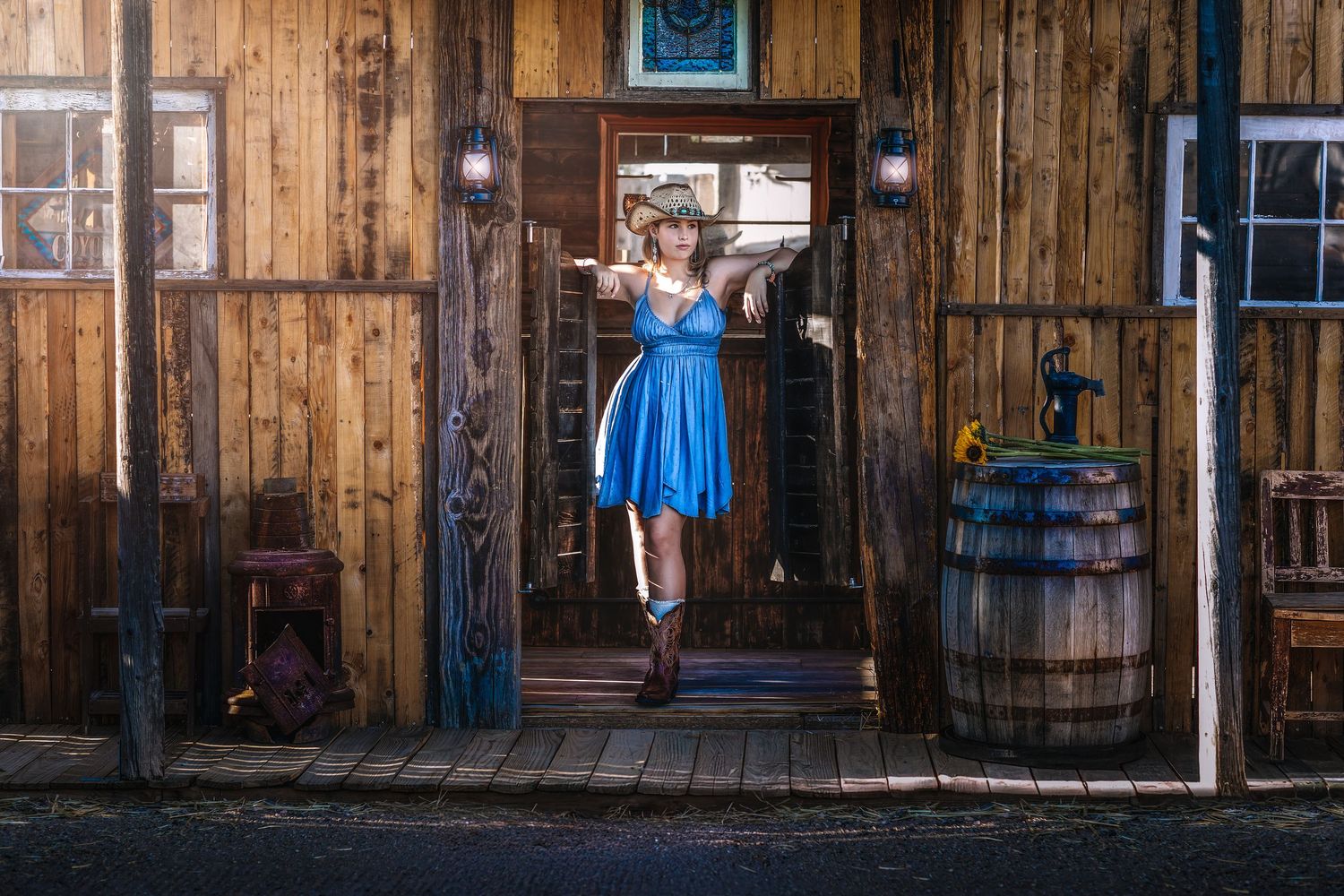 Woman in blue dress and cowboy boots standing in doorway of western wooden building.