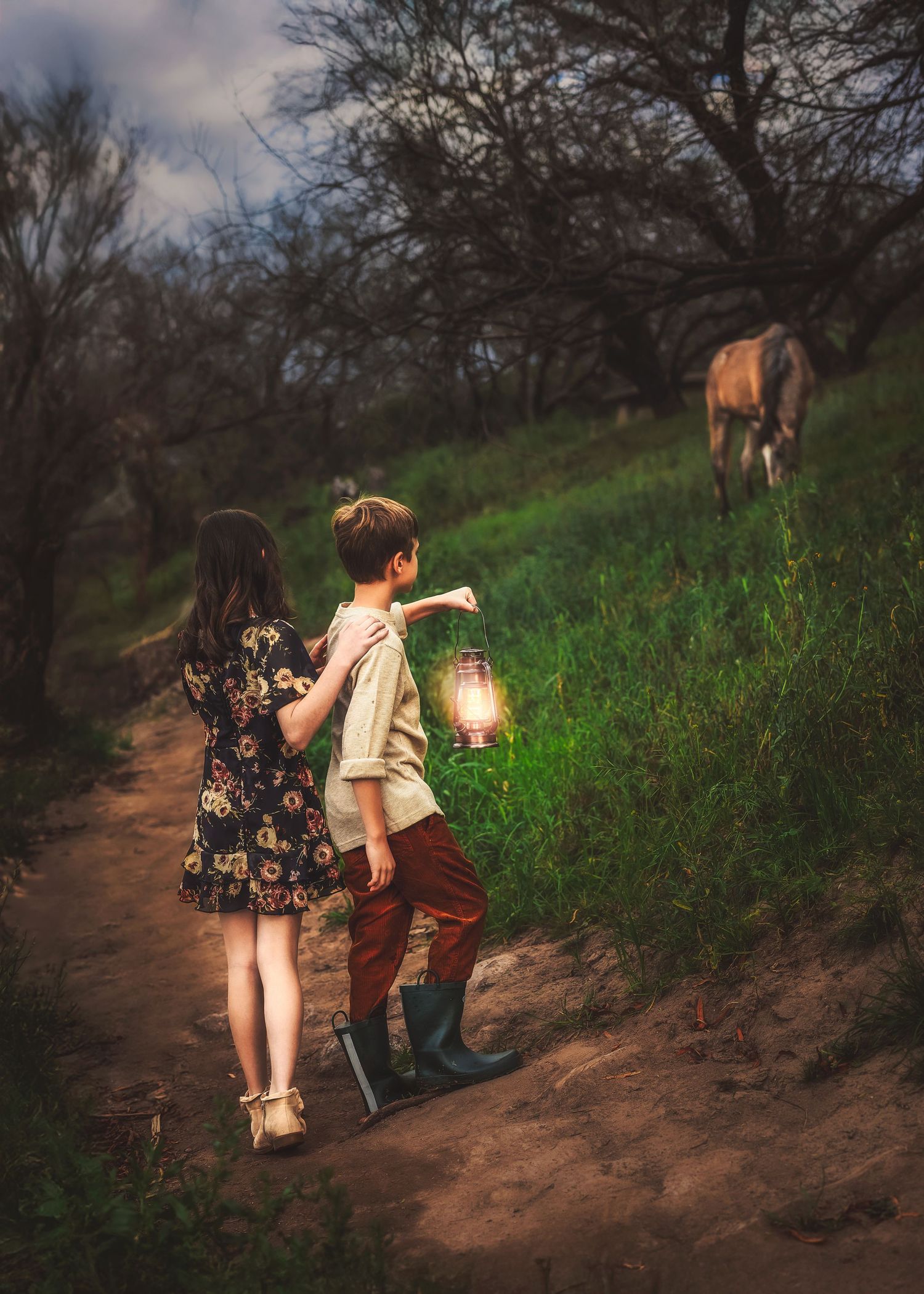 Two children walk a dirt path toward a horse at dusk, boy carrying a glowing vintage lantern in a forest.