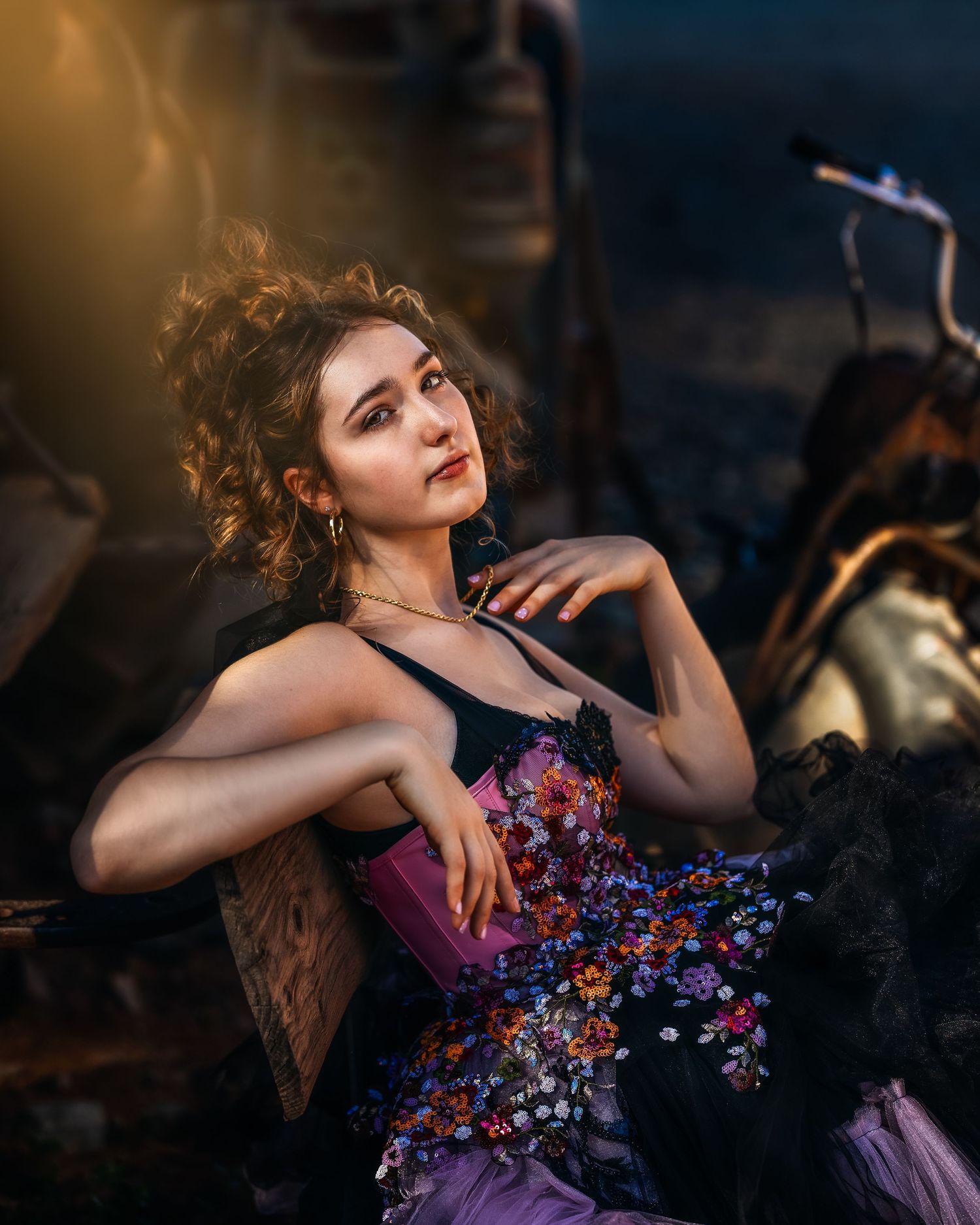 Young woman in floral embroidered purple dress poses outdoors in golden hour light.