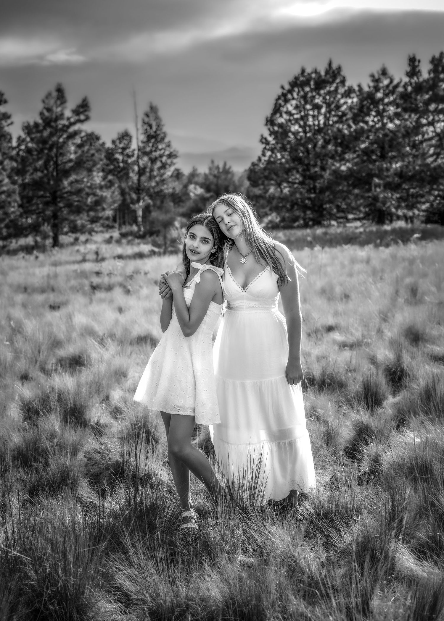 Two women in white dresses posing in a field at dusk, black and white photo.
