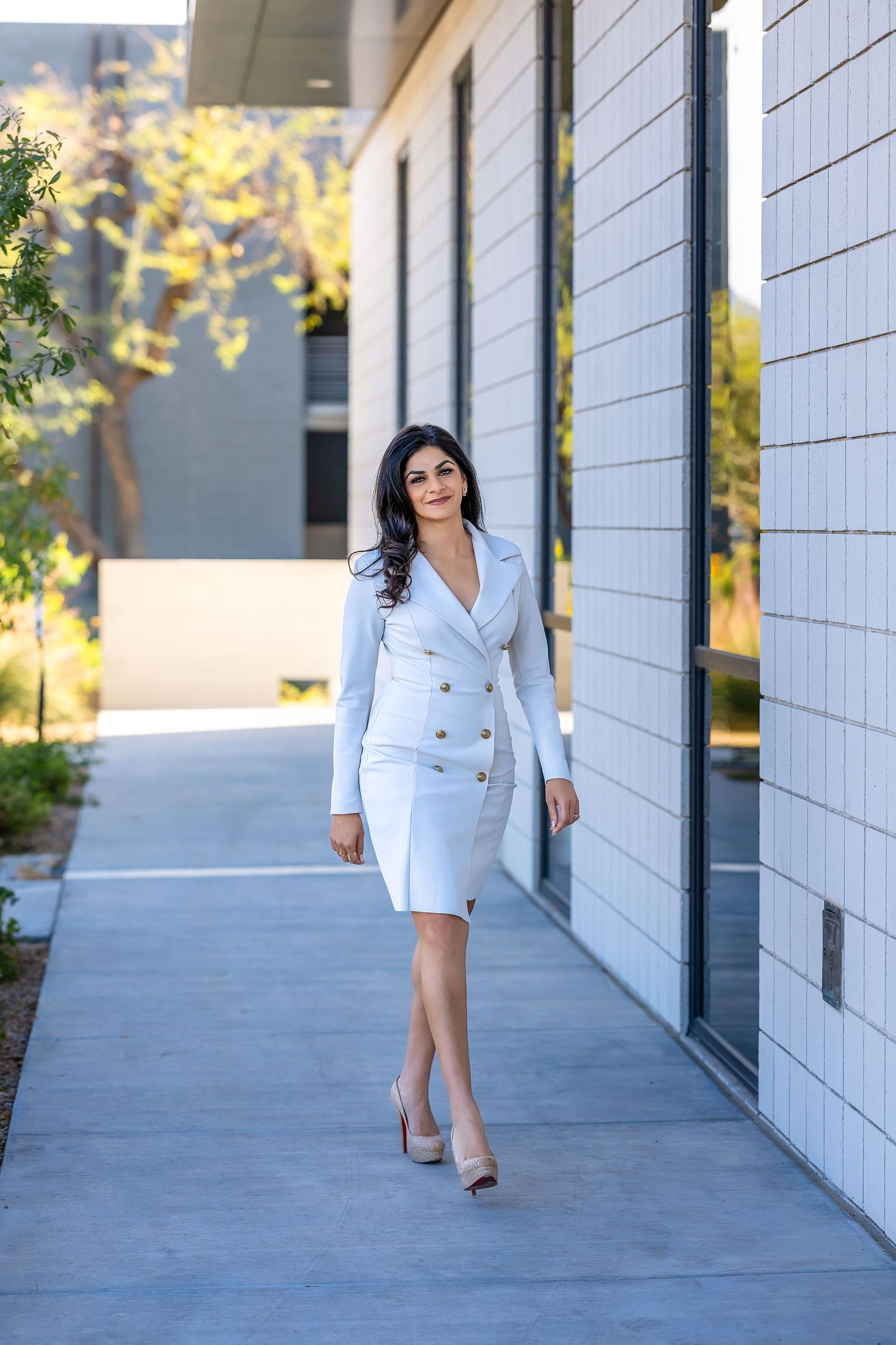 Powerful CEO and female entrepreneur walking in front of mirrored windows wearing a white coat dress.