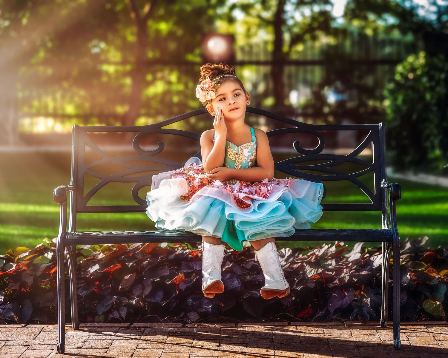 A young girl in a colorful ruffled dress sits thoughtfully on a park bench in golden sunlight.