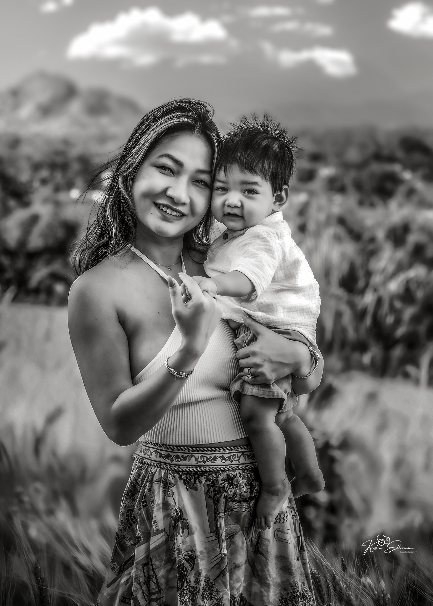 Black and white portrait of a smiling young Asian woman holding a happy baby outdoors in a field.