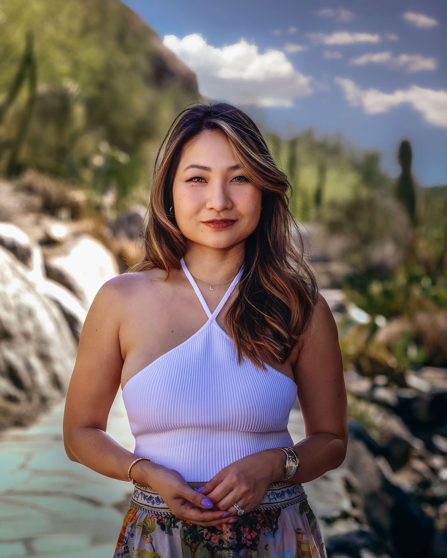 Portrait of a woman in a white ribbed halter top and floral skirt posing in a desert garden setting.