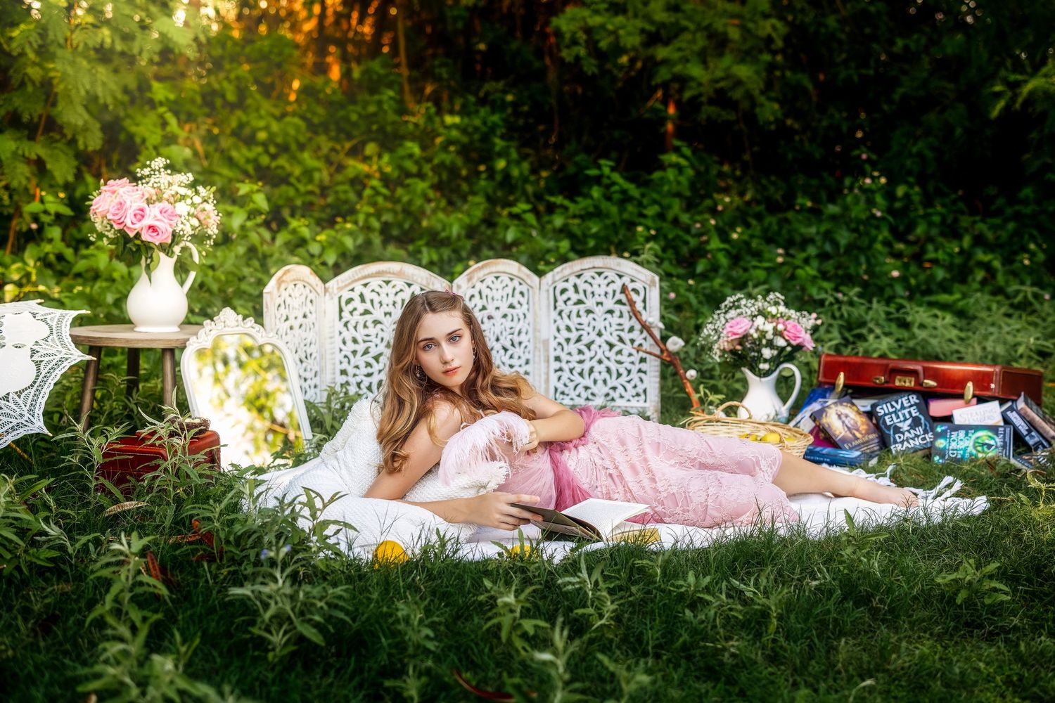 Young girl relaxing on white ornate outdoor sofa surrounded by flowers and greenery in a garden setting.