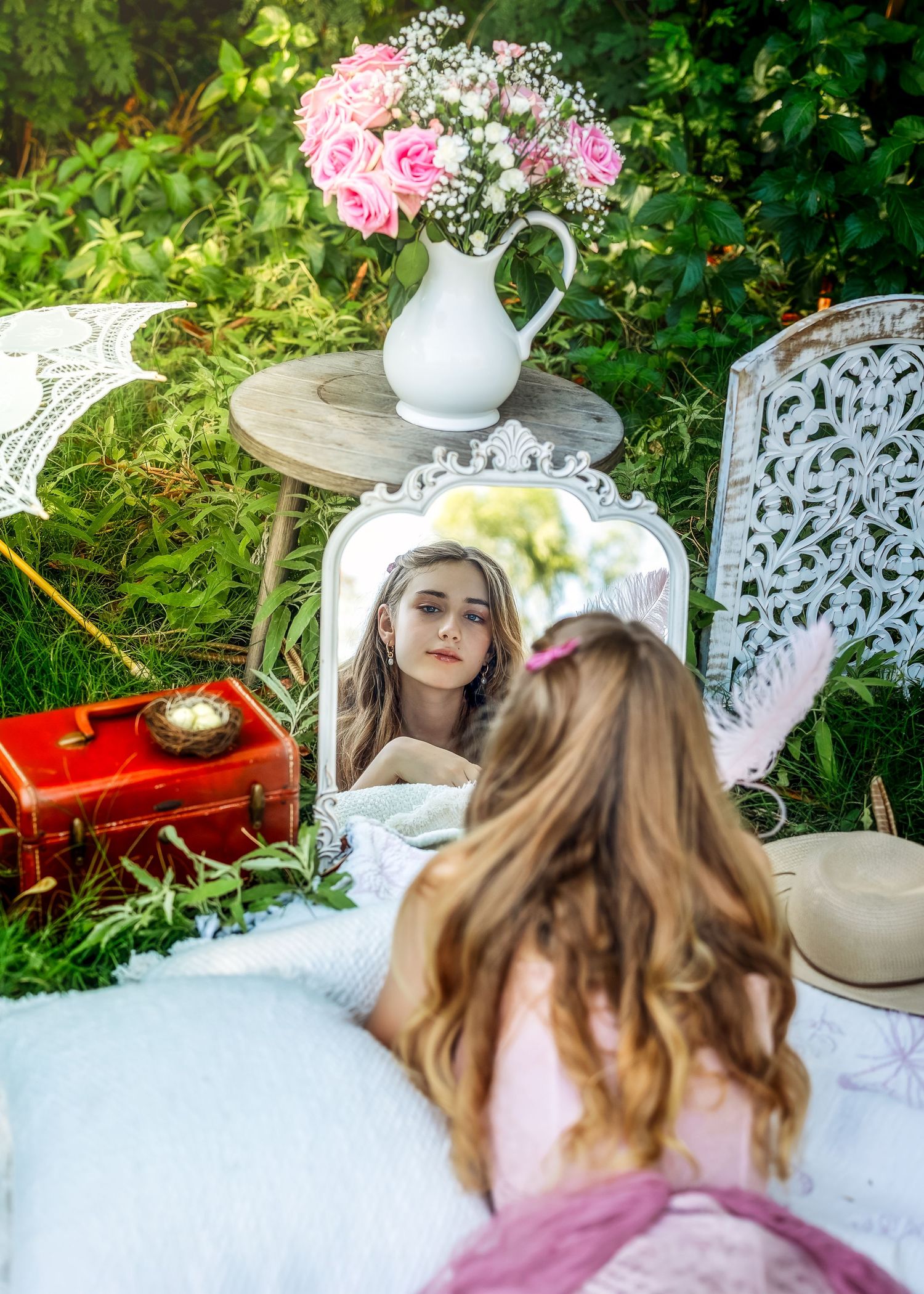Young woman with flower crown gazes at her reflection in ornate mirror surrounded by roses and vintage decor outdoors.