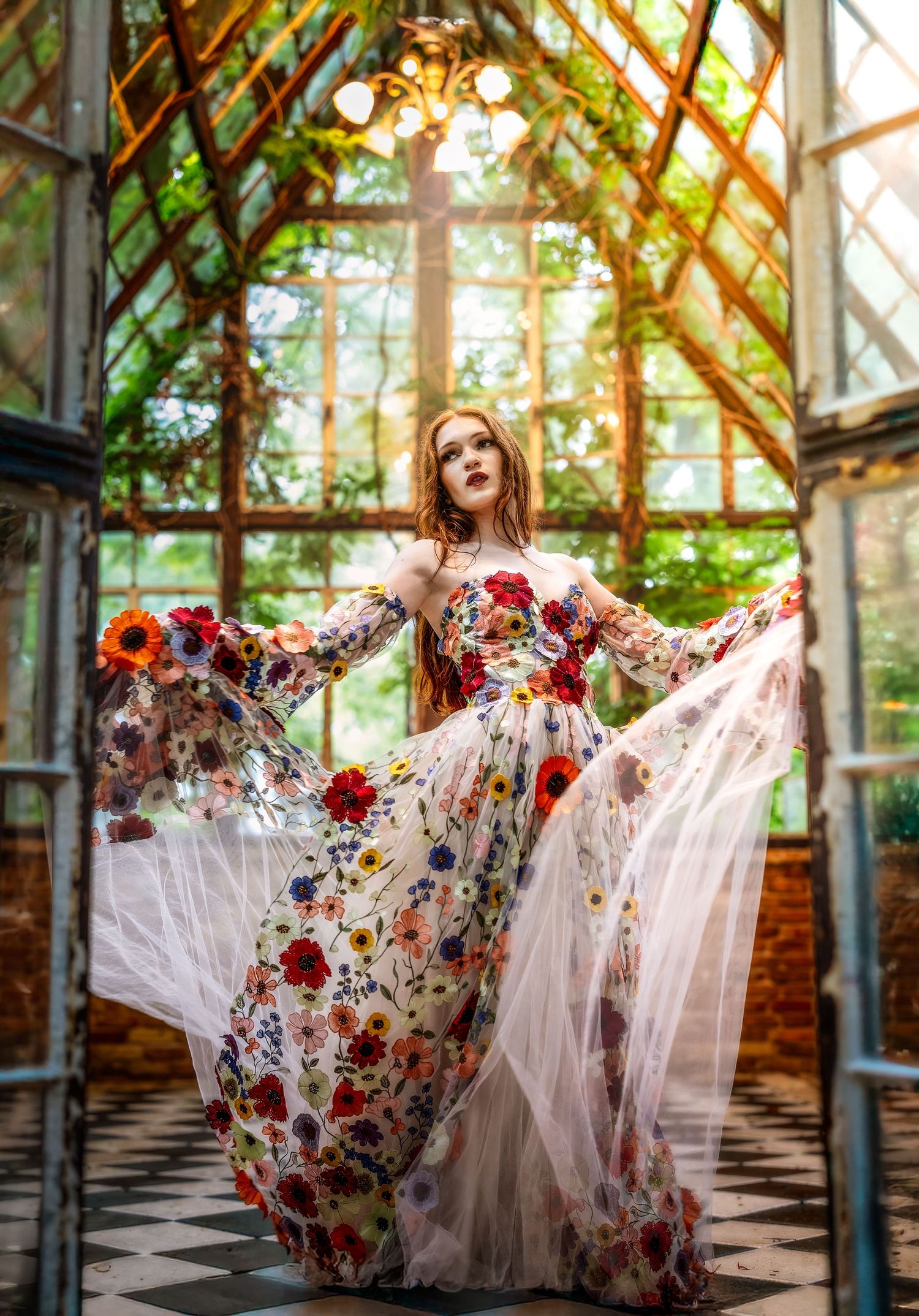A woman in a floral tulle gown poses gracefully in a sunlit greenhouse with lush greenery.